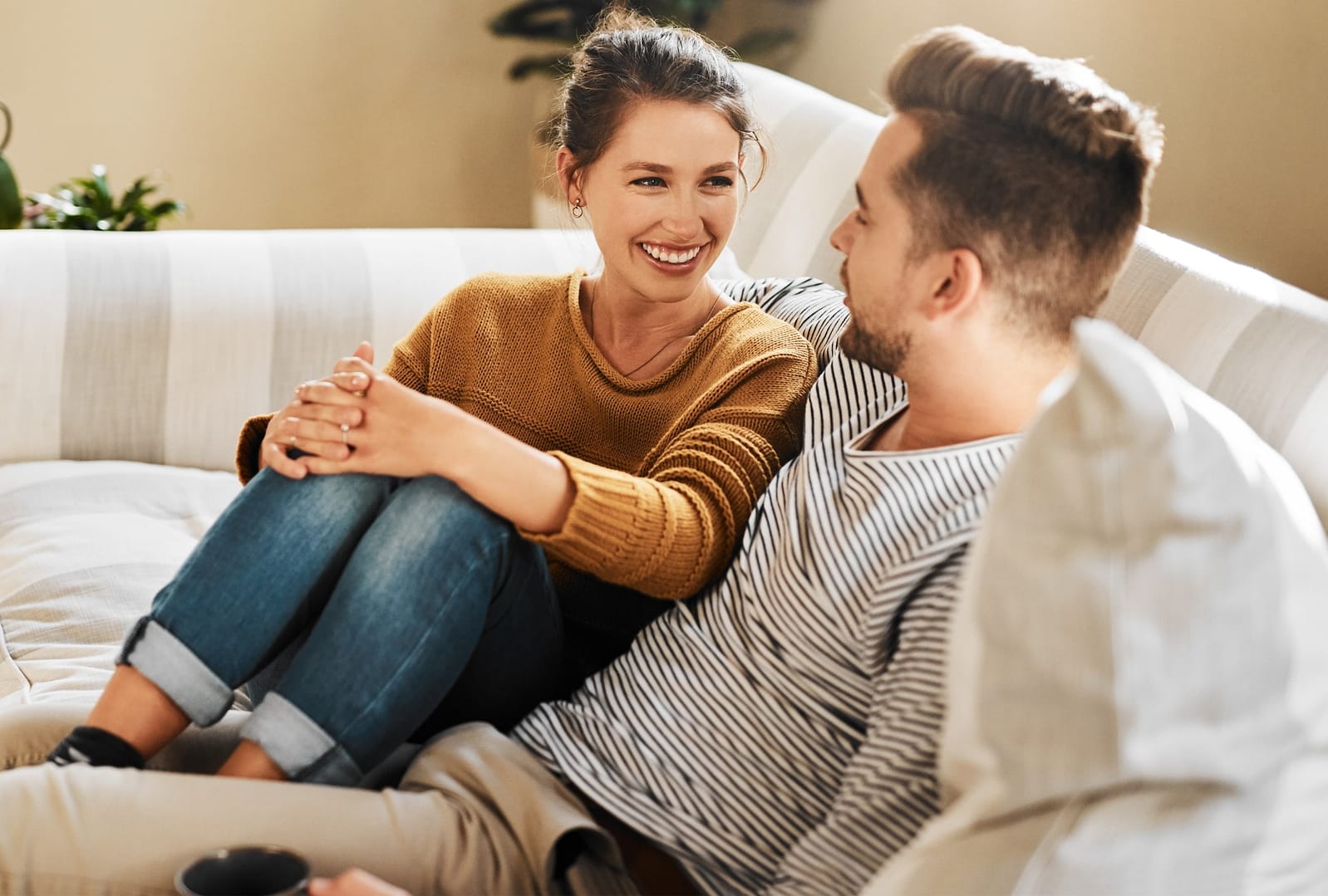 A woman and a man sit on a couch facing each other, smiling and talking in a bright living room as they communicate with your husband openly and happily.