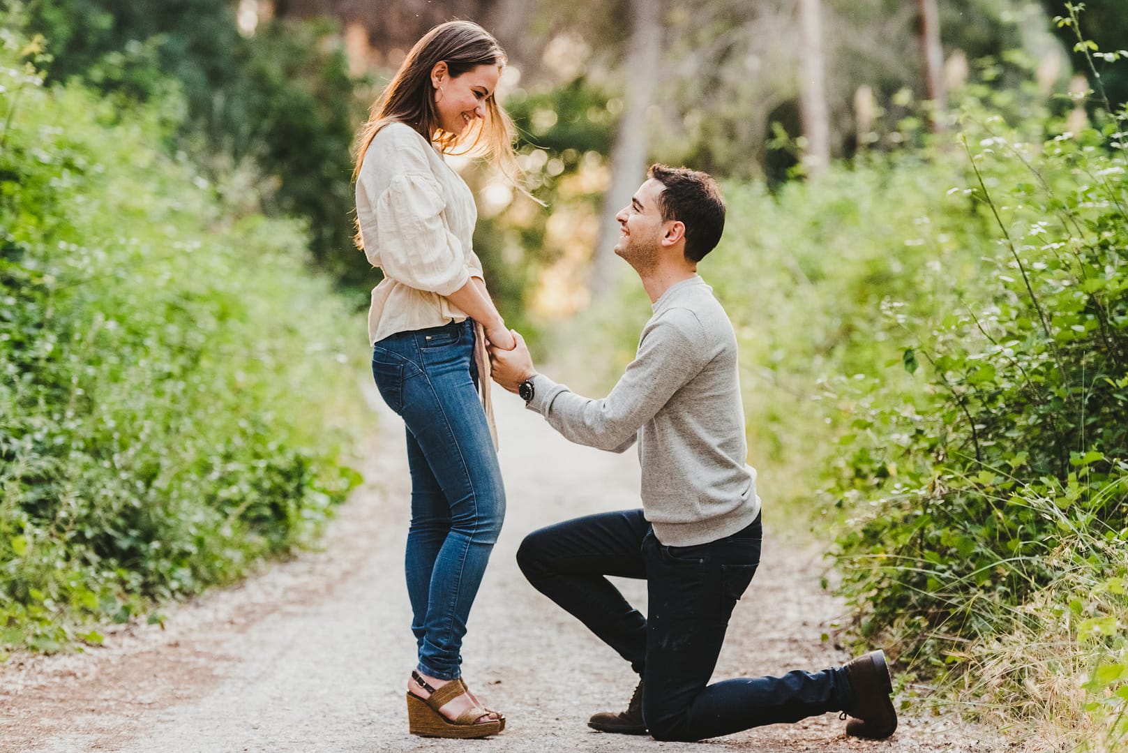 A man kneels on one knee holding hands with a woman, proposing to her on a forest path—a touching moment of hope and renewal for marriage after betrayal. Marriage recovery