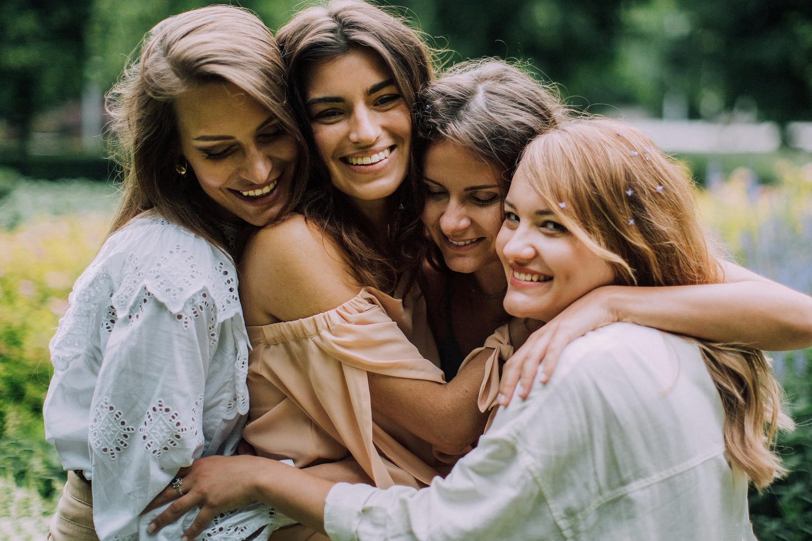Four young women stand closely together outdoors, smiling and hugging each other amidst greenery—a perfect moment for quotes for women embracing change.