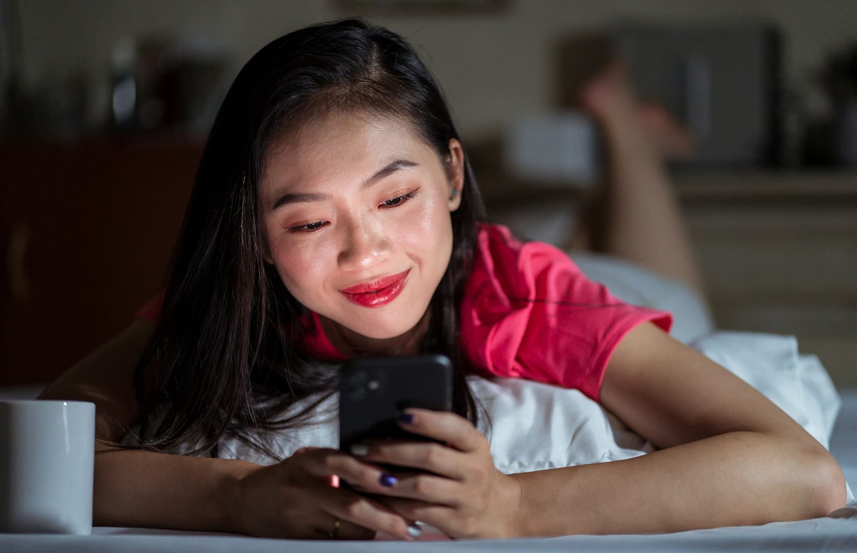 Young woman in bed smiling at her phone, capturing the “Yearners” trend of heartfelt, authentic texting.