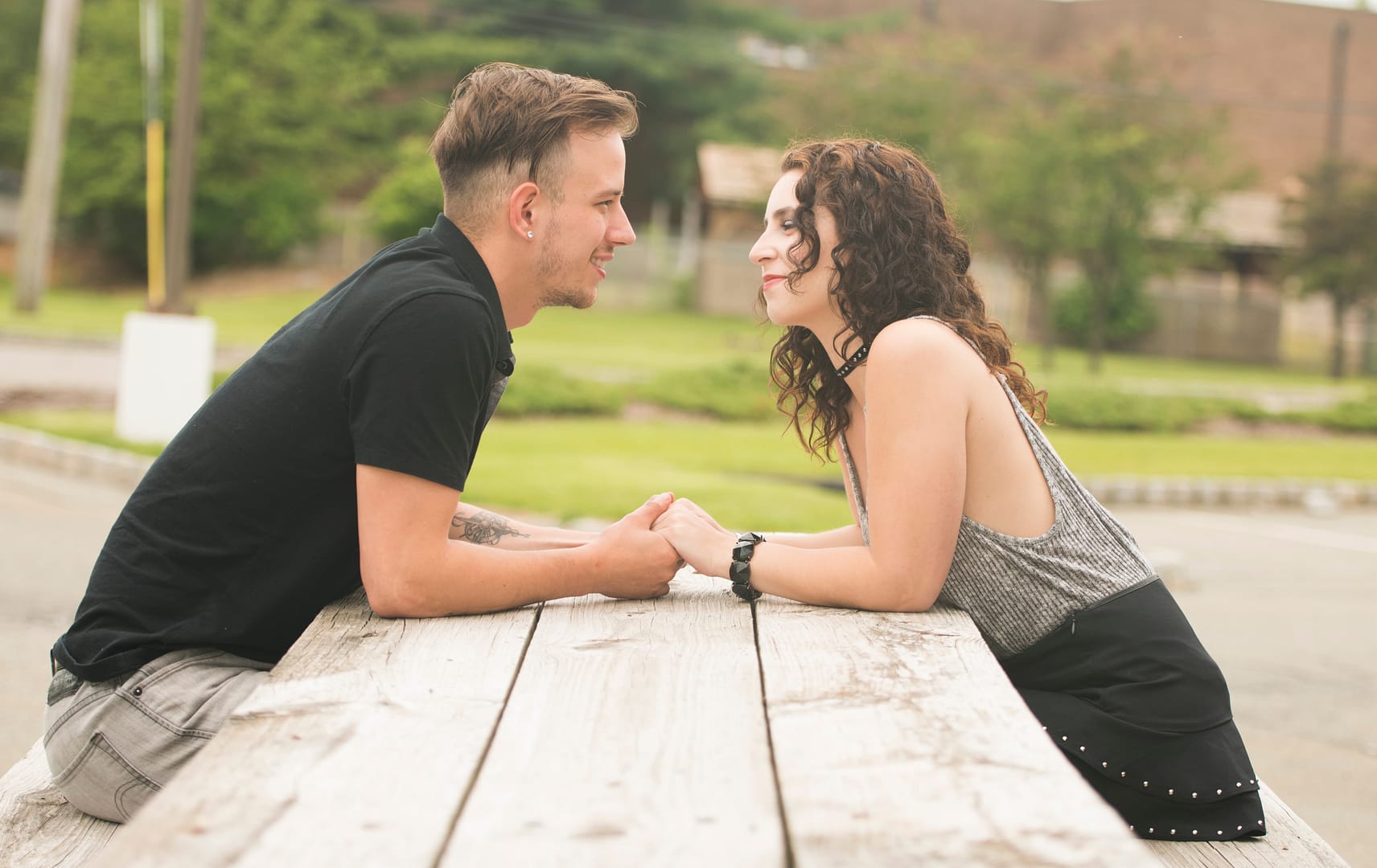 Two people sit across from each other at a wooden picnic table outdoors, holding hands and making eye contact. How to fix communication in a relationship
