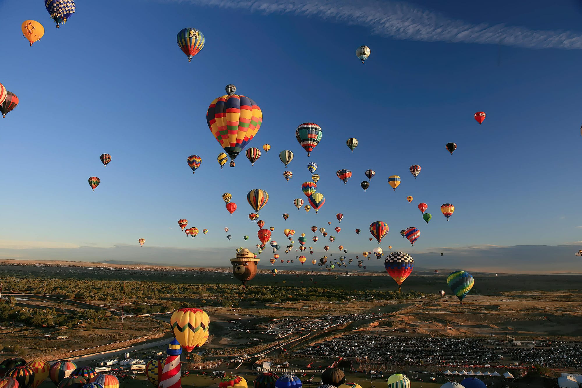 Dozens of brightly colored hot air balloons float in the sky over a large, open landscape during Balloon Fiesta 2007 in Albuquerque