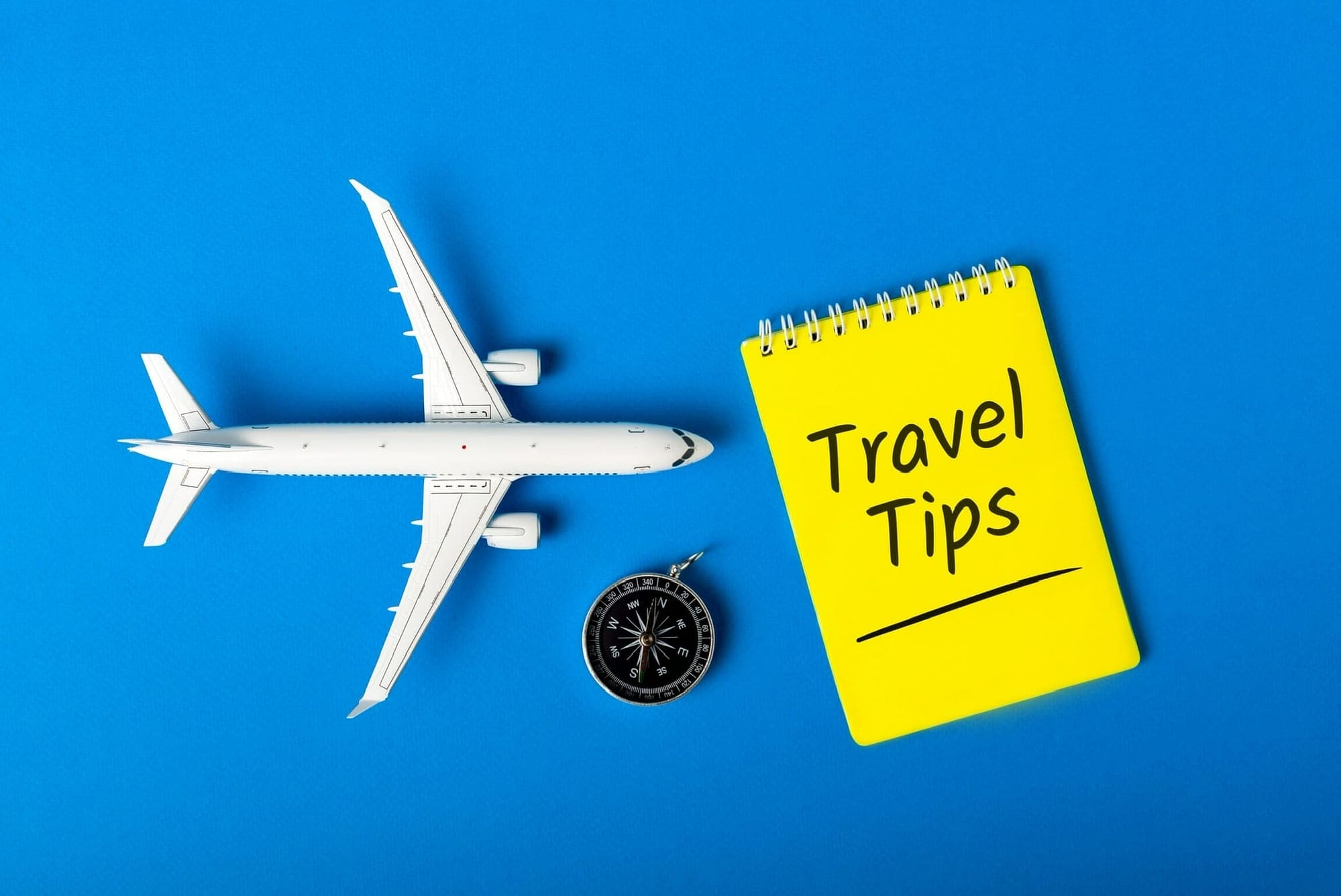 Notepad, compas and toy airplane on blue background. Summer travel concept