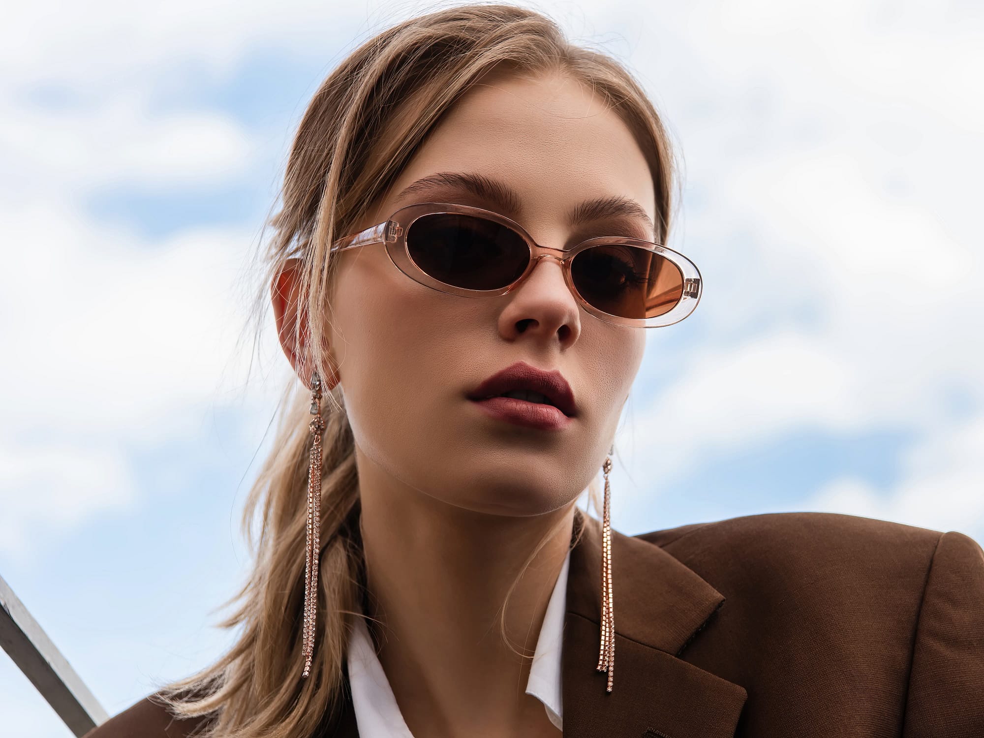 Young woman in sunglasses and blazer posing against blue sky