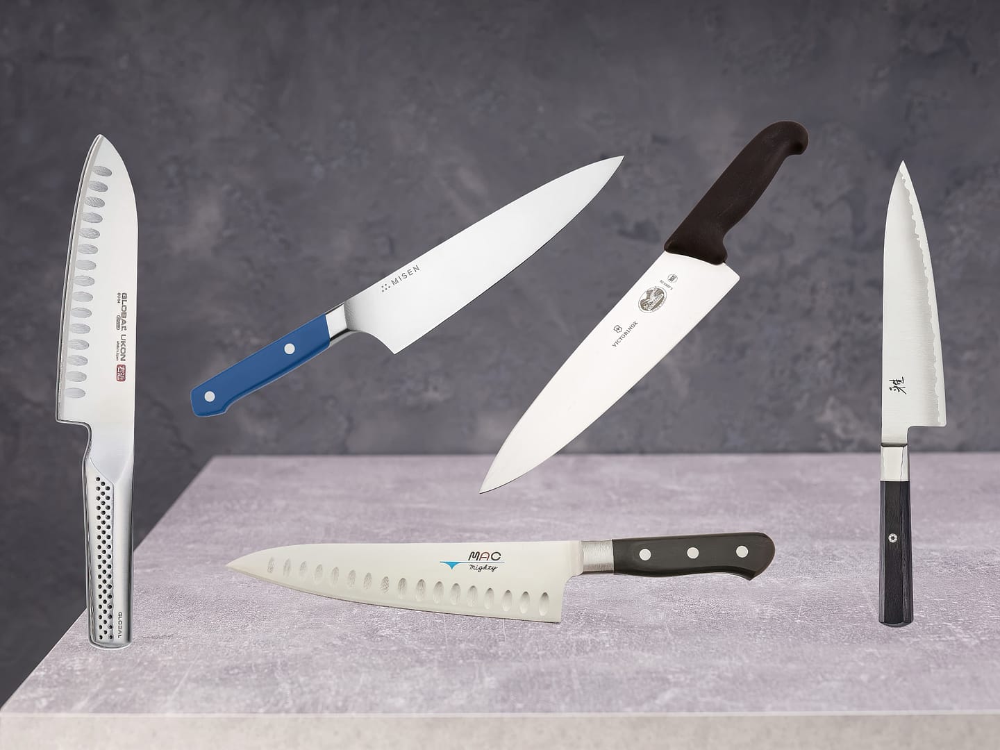 Five different chef's knives, among the best kitchen knives, displayed against a grey backdrop