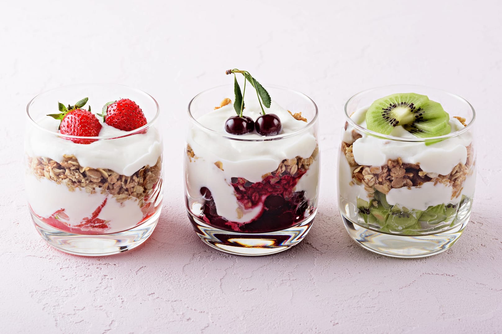 Vegetarian desserts with cottage cheese, granola, strawberry, cherry, kiwi on pink background