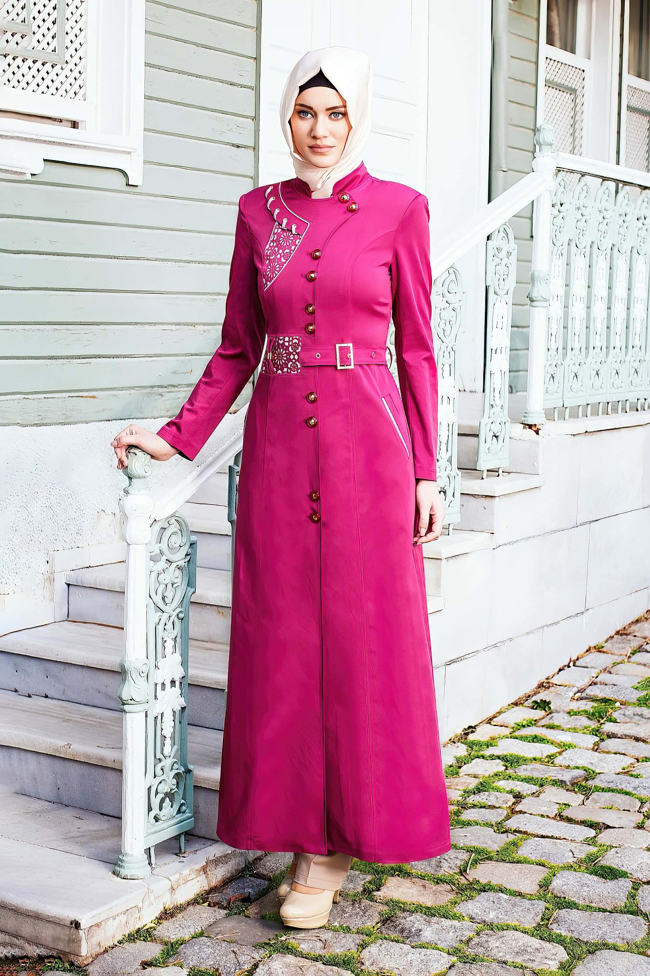 Woman in a long pink coat stands in front of a house