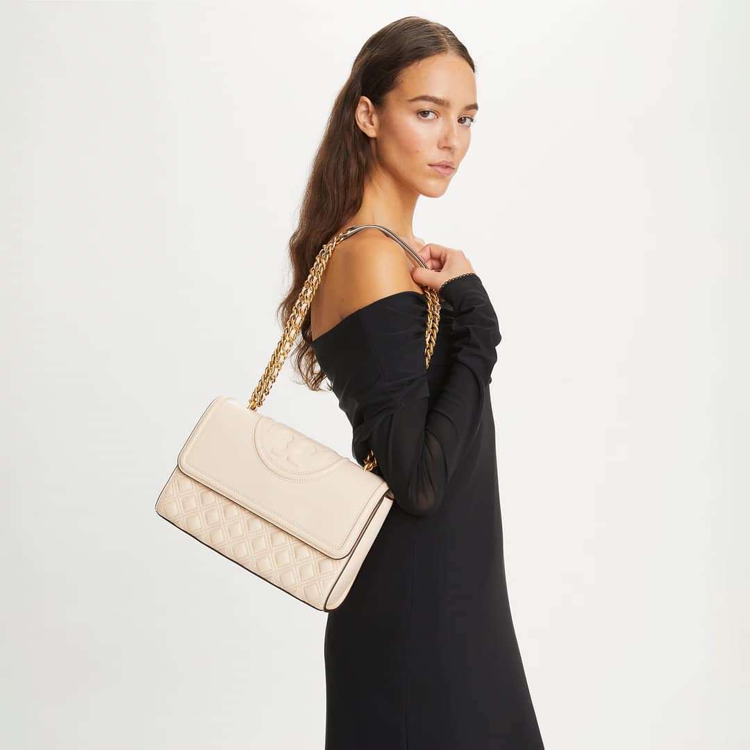 Female model posing with Tory Burch Fleming Quilted Leather Convertible Shoulder Bag against a plain gray backdrop