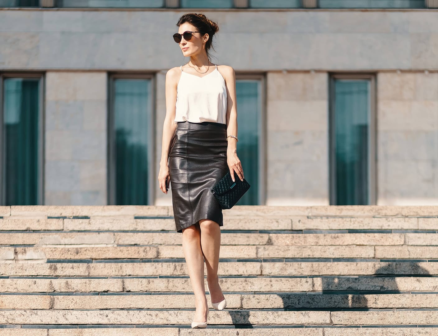 Fashionable brunette businesswoman in leather pencil skirt and sunglasses walking on stairs