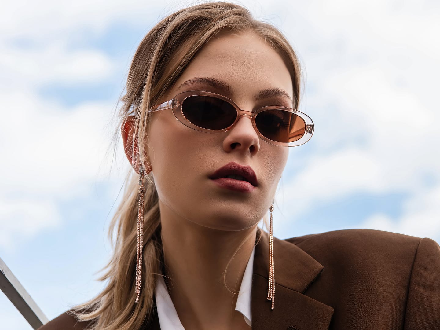 Young woman in sunglasses and blazer posing against blue sky