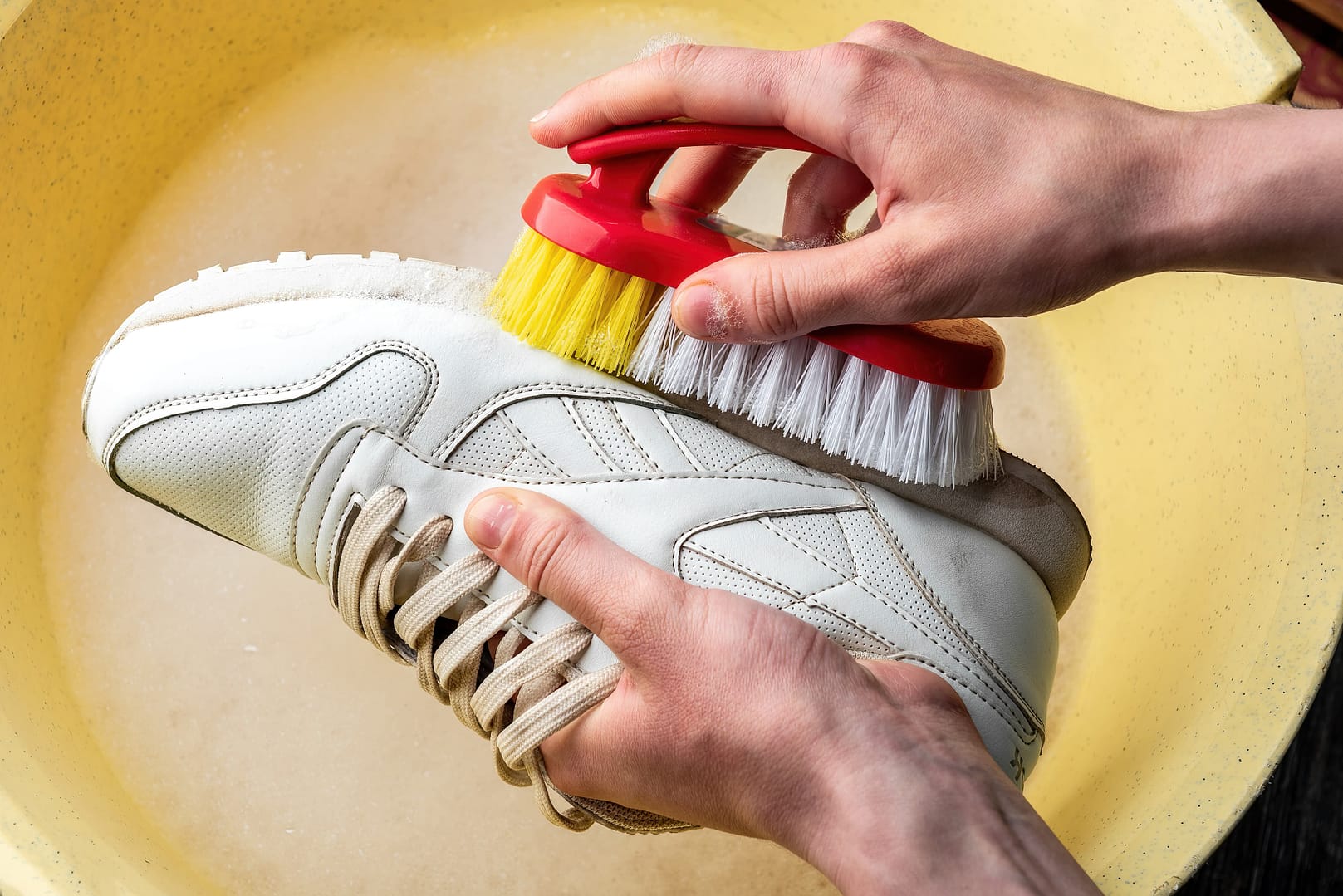 Close-up of hands of a person cleaning a white sneaker using a scrubbing brush