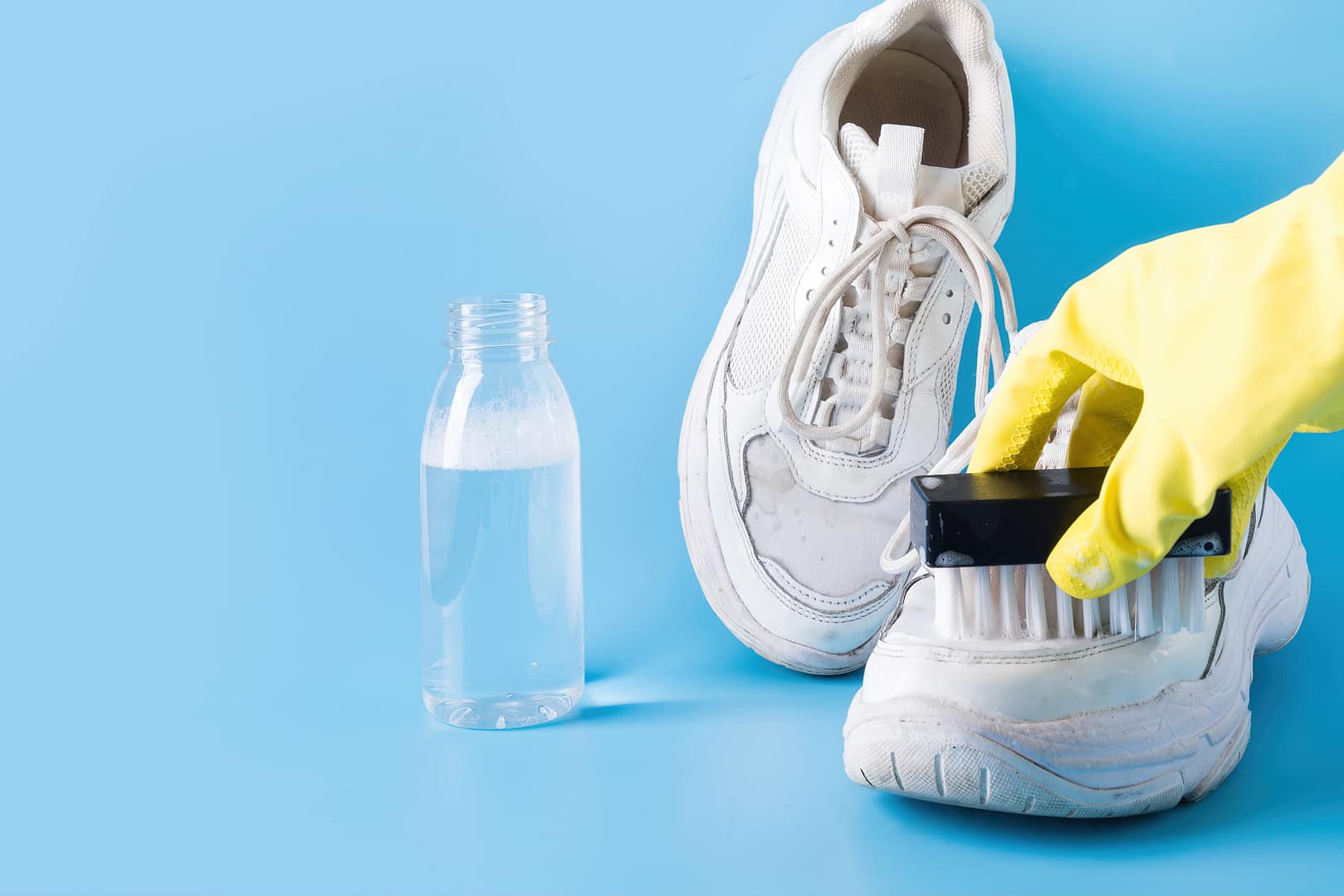 Dirty white sneakers with special tool for cleaning them on blue