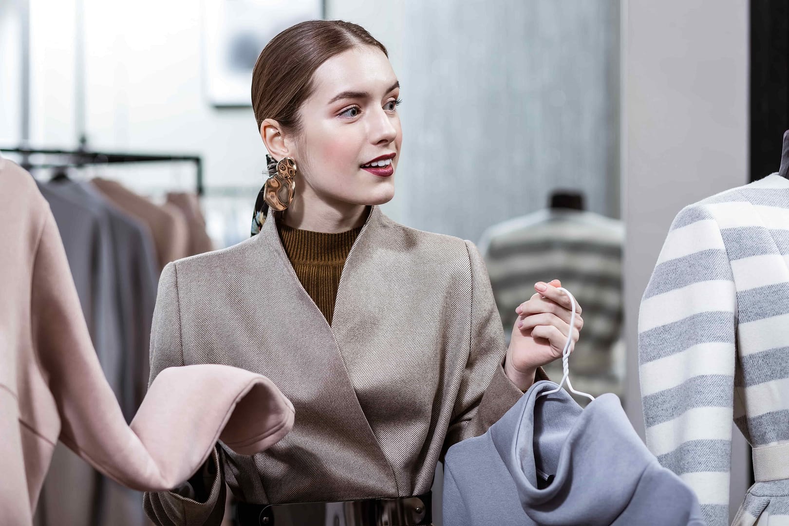 Stylish long-haired young smiling woman wearing big earrings looking thoughtful