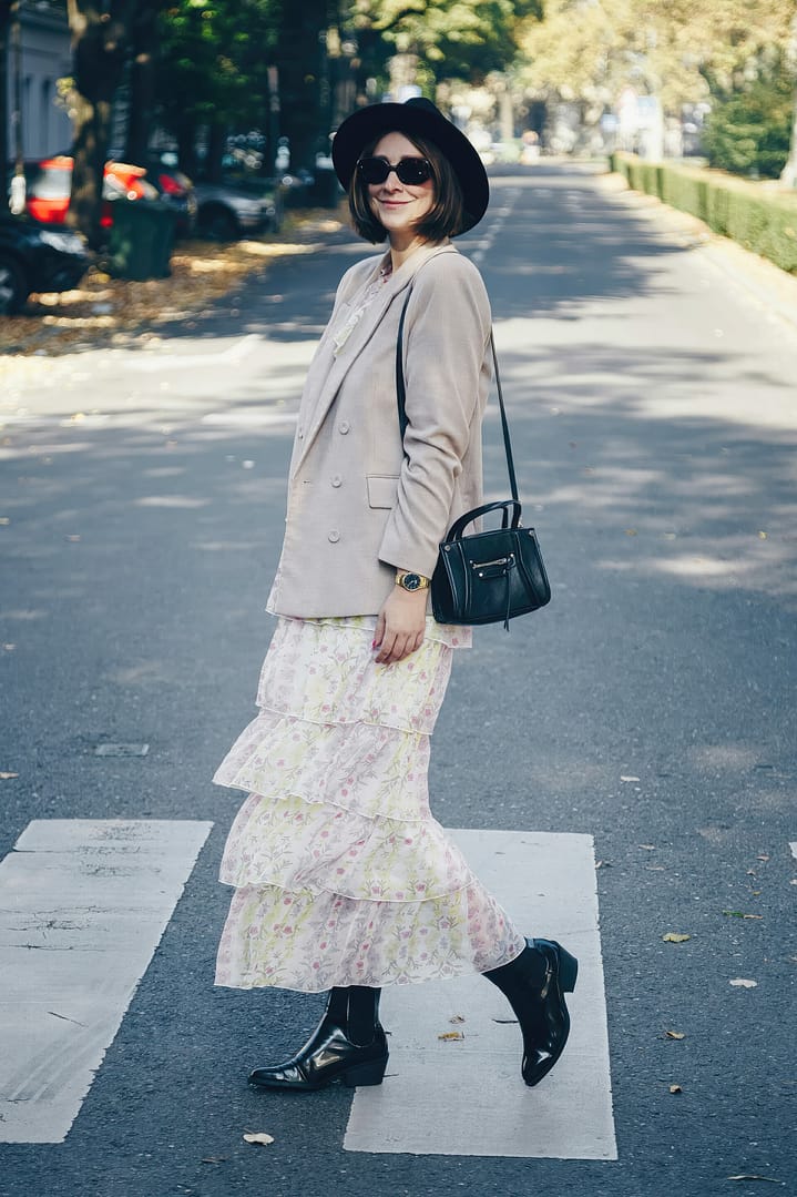 Fashion blogger street style. Fashionable woman posing wearing an oversized blazer, floral vintage dress, black ankle boots and a black trendy mini handbag