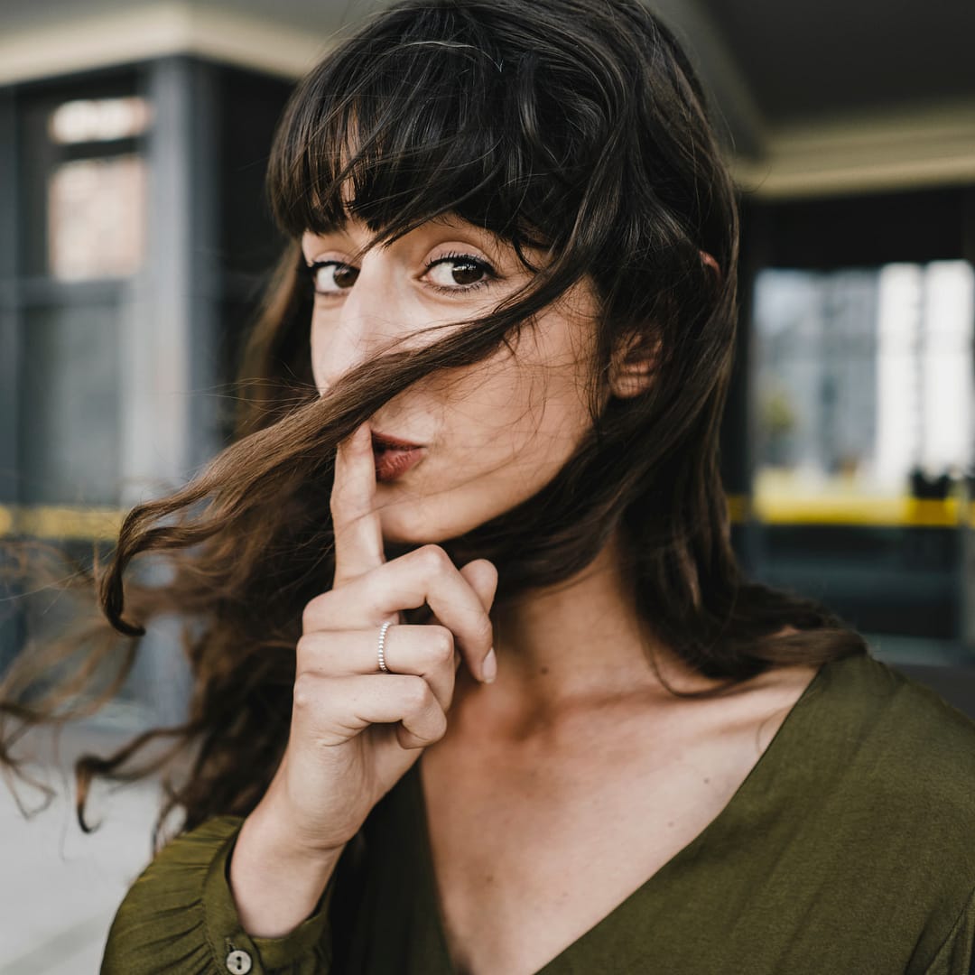 Portrait of smiling brunette woman, finger on mouth