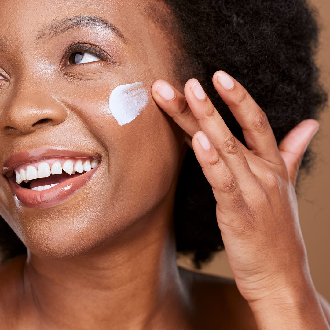 African American woman smiles gently while applying an acne spot treatment cream to her cheek