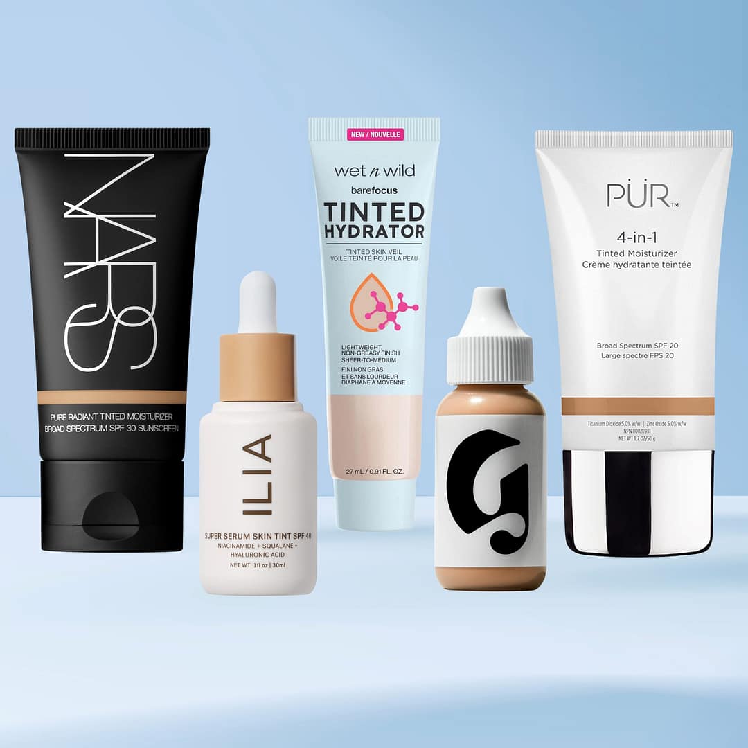 Five bottles of the best tinted moisturizers from different brands are displayed in a row against a light blue gradient background. Each product container varies in design, shape, and color
