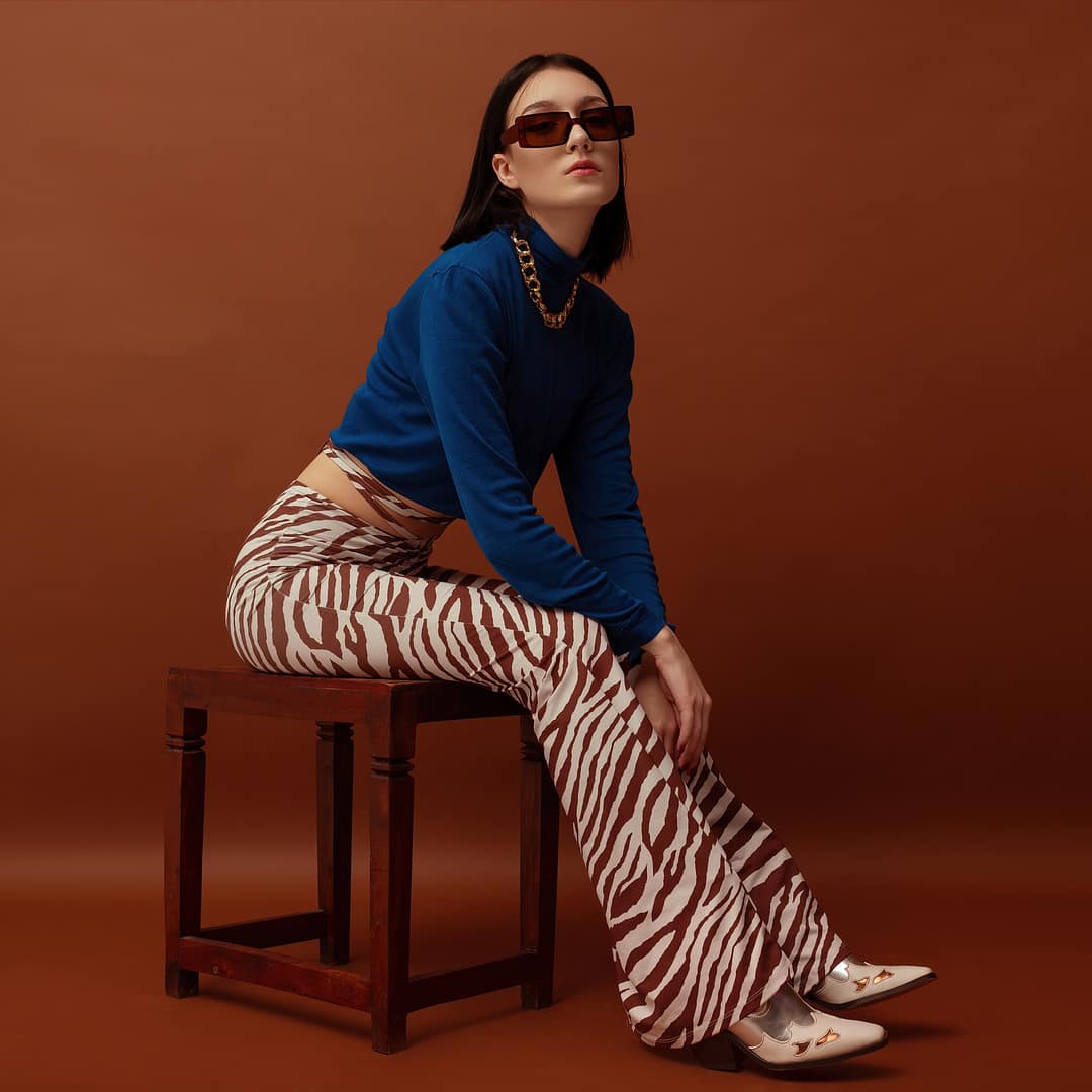 Fashionable woman wearing trendy brown rectangular sunglasses, stylish blue turtleneck, flared trousers with zebra print, and boots