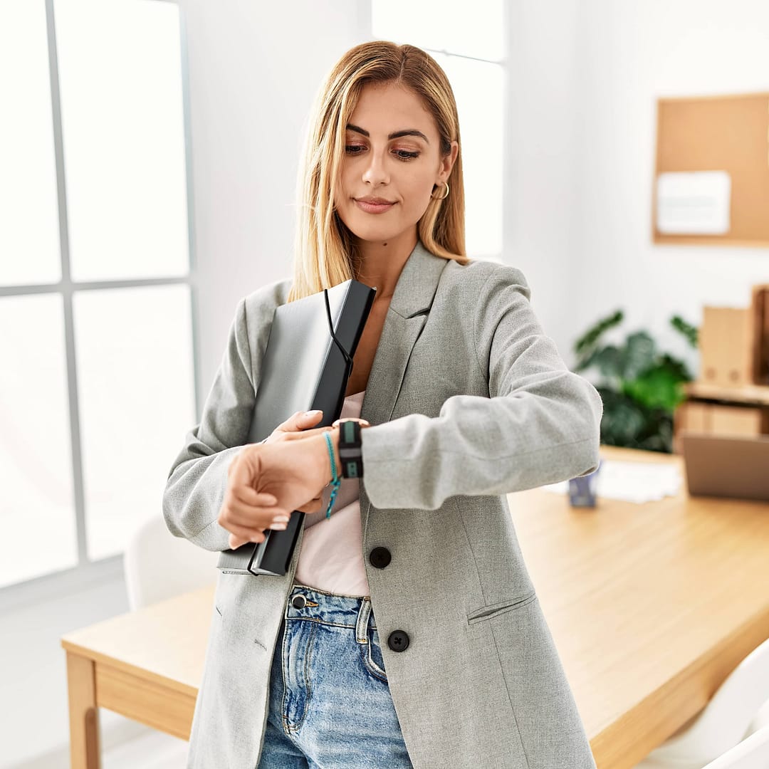 Blonde business woman at the office checking the time on wrist watch, relaxed and confident