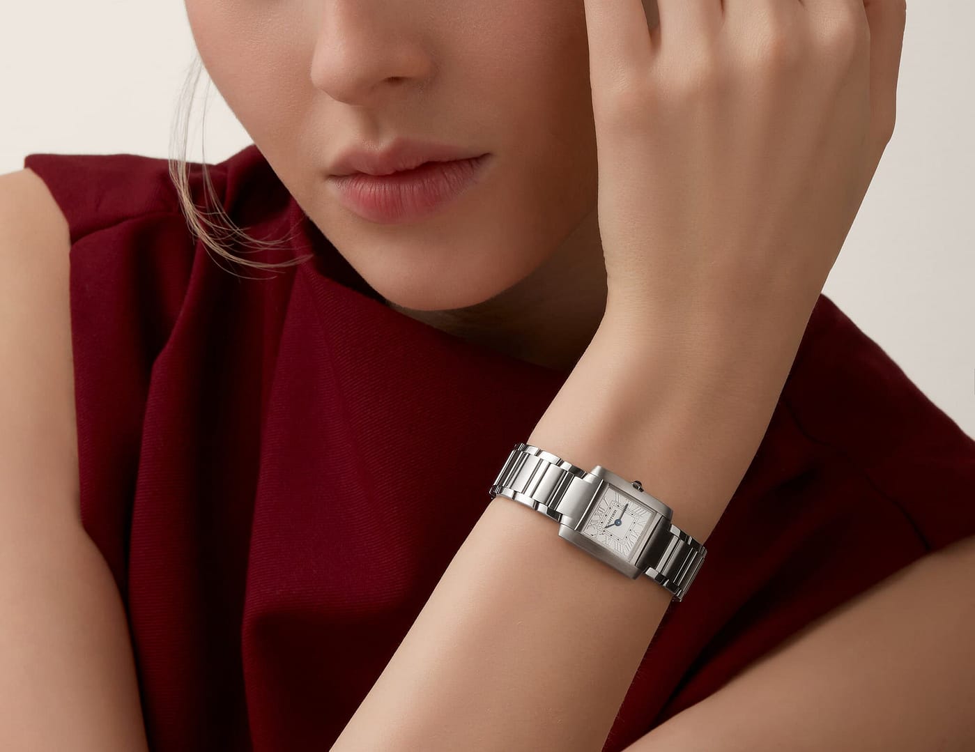 Woman wearing a silver Cartier Tank Francaise Silver Dial Watch, resting her chin on her hand, dressed in a burgundy top