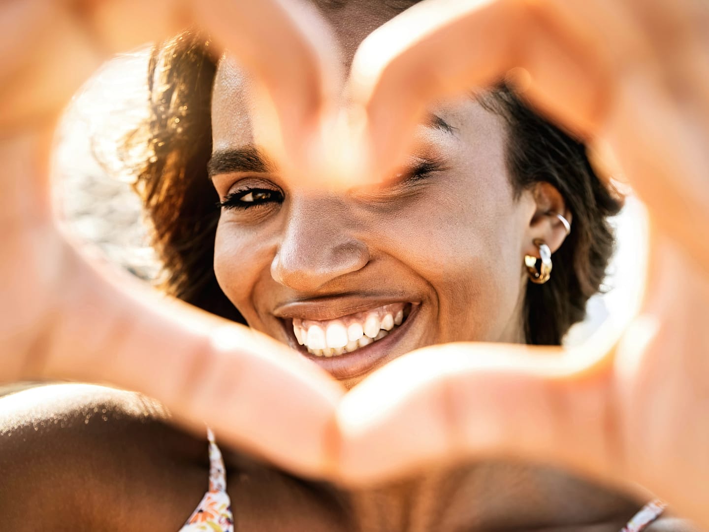 Close up image of smiling woman in swimwear on the beach making a heart shape with hands