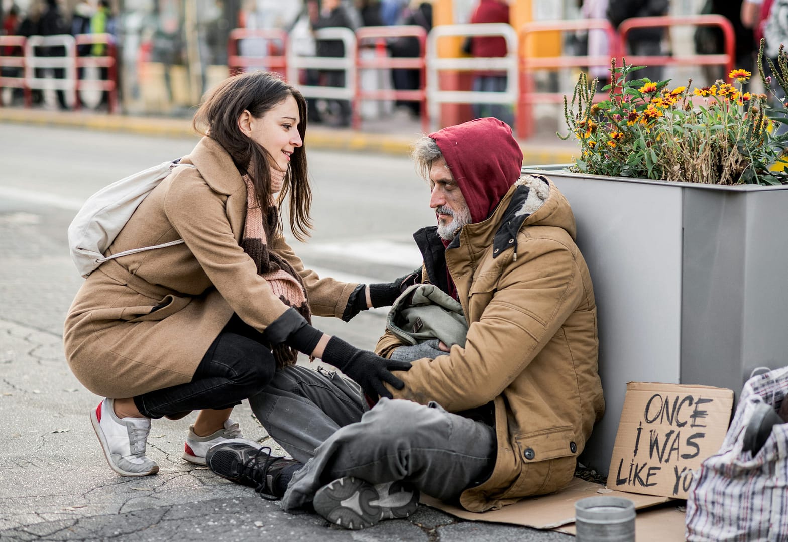 Young woman giving money to homeless beggar man sitting in city