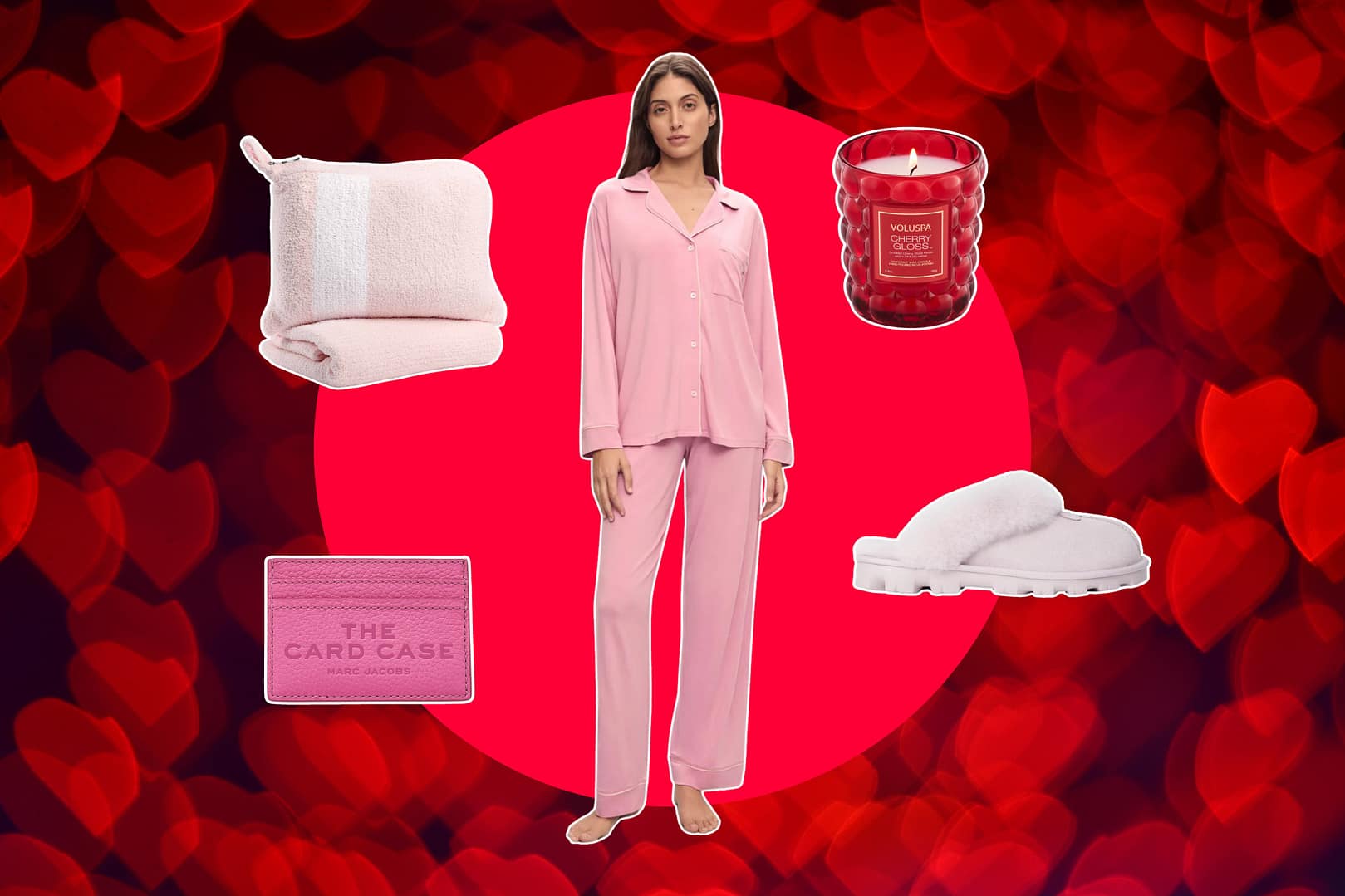 Woman stands against a red heart-patterned background, surrounded by thoughtful Valentine's Day gifts for her: a pink travel blanket, red candle, pink card case, cozy pink slippers and pink pajamas that she's wearing