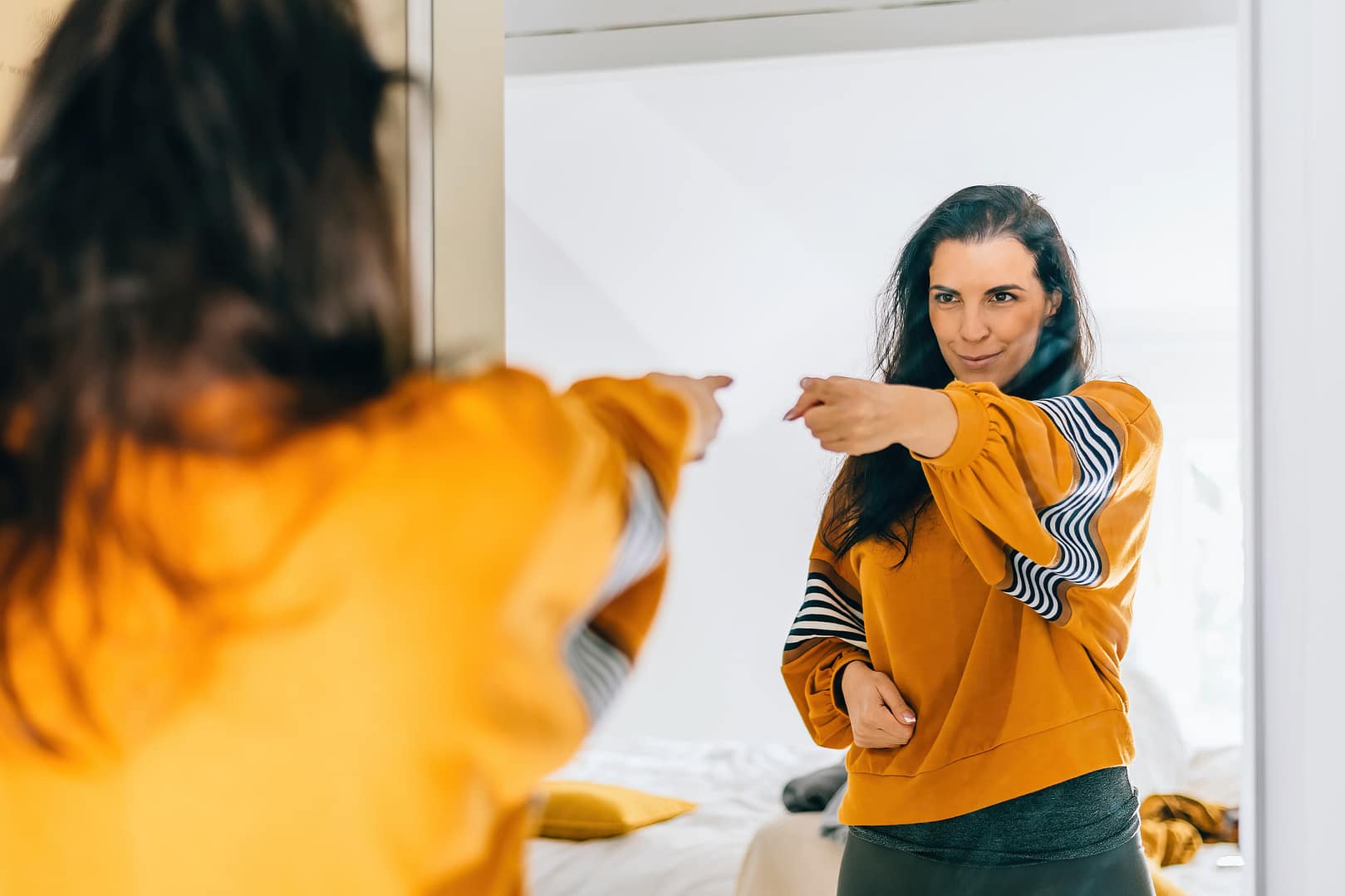 Self confident woman pointing finger at reflection in mirror dancing and feeling good