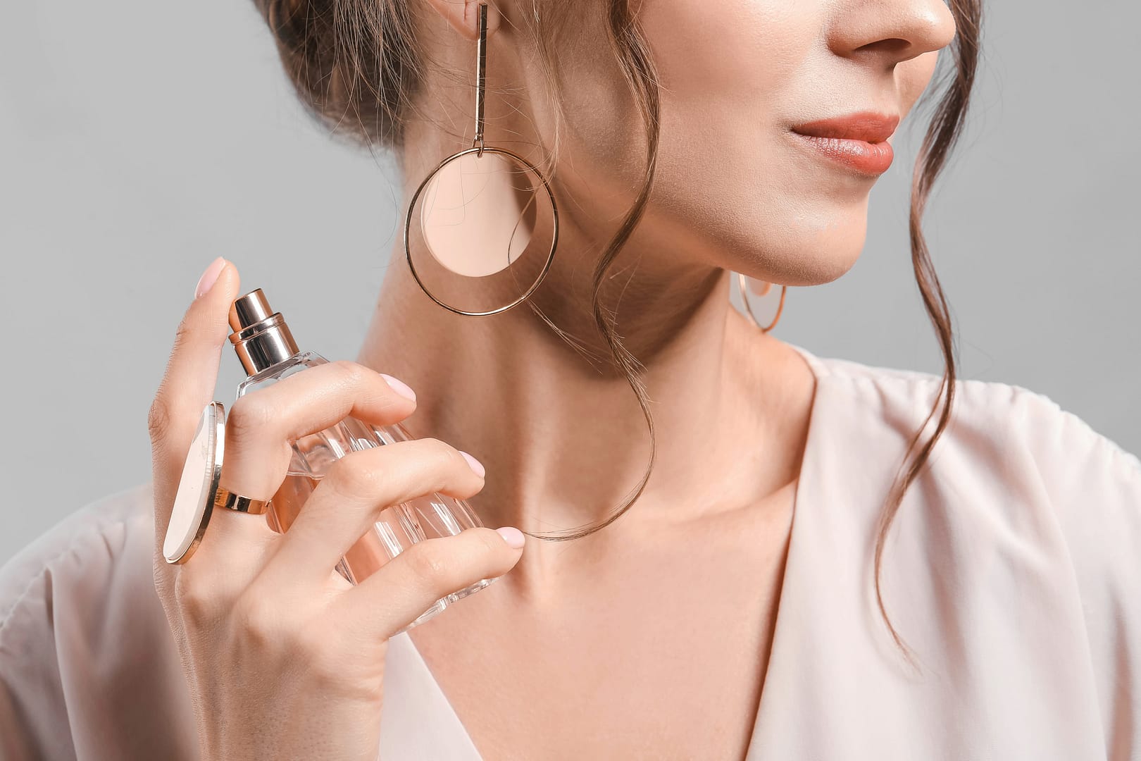 Beautiful young woman with bottle of perfume on grey background