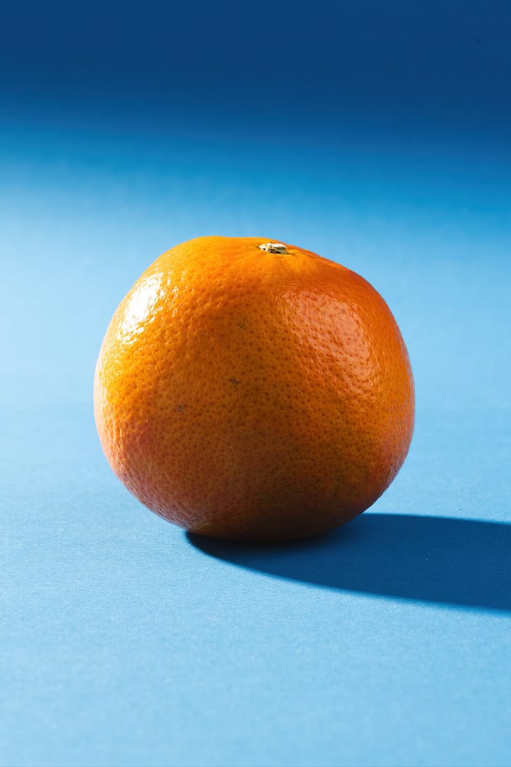 Orange for glowing skin. A single orange positioned on a blue background with a shadow cast to the right