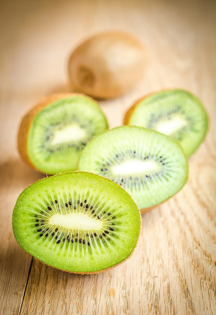 Four sliced kiwis on a wooden surface, showcasing their green interior and black seeds