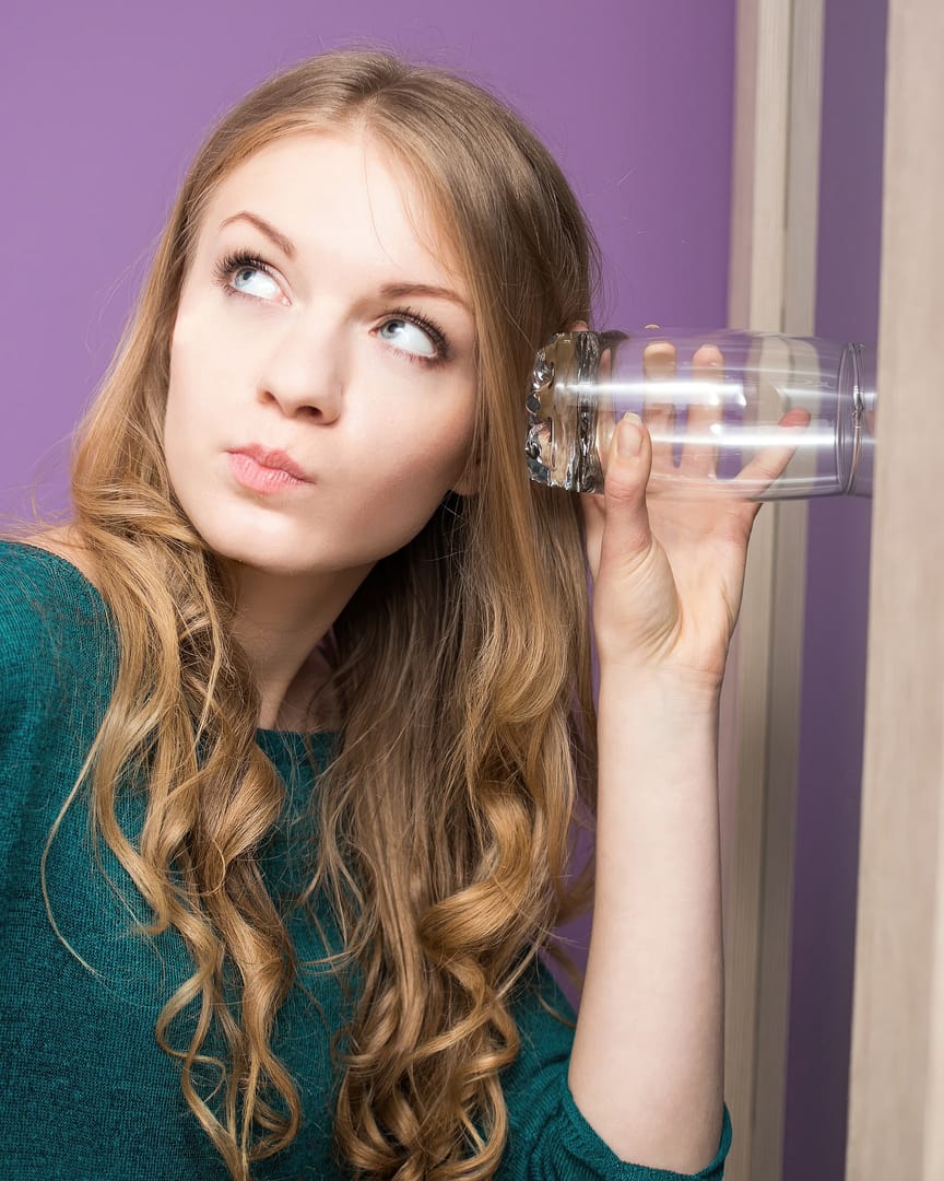 Curious young woman with glass being nosy and eavesdropping her neighbor's conversations