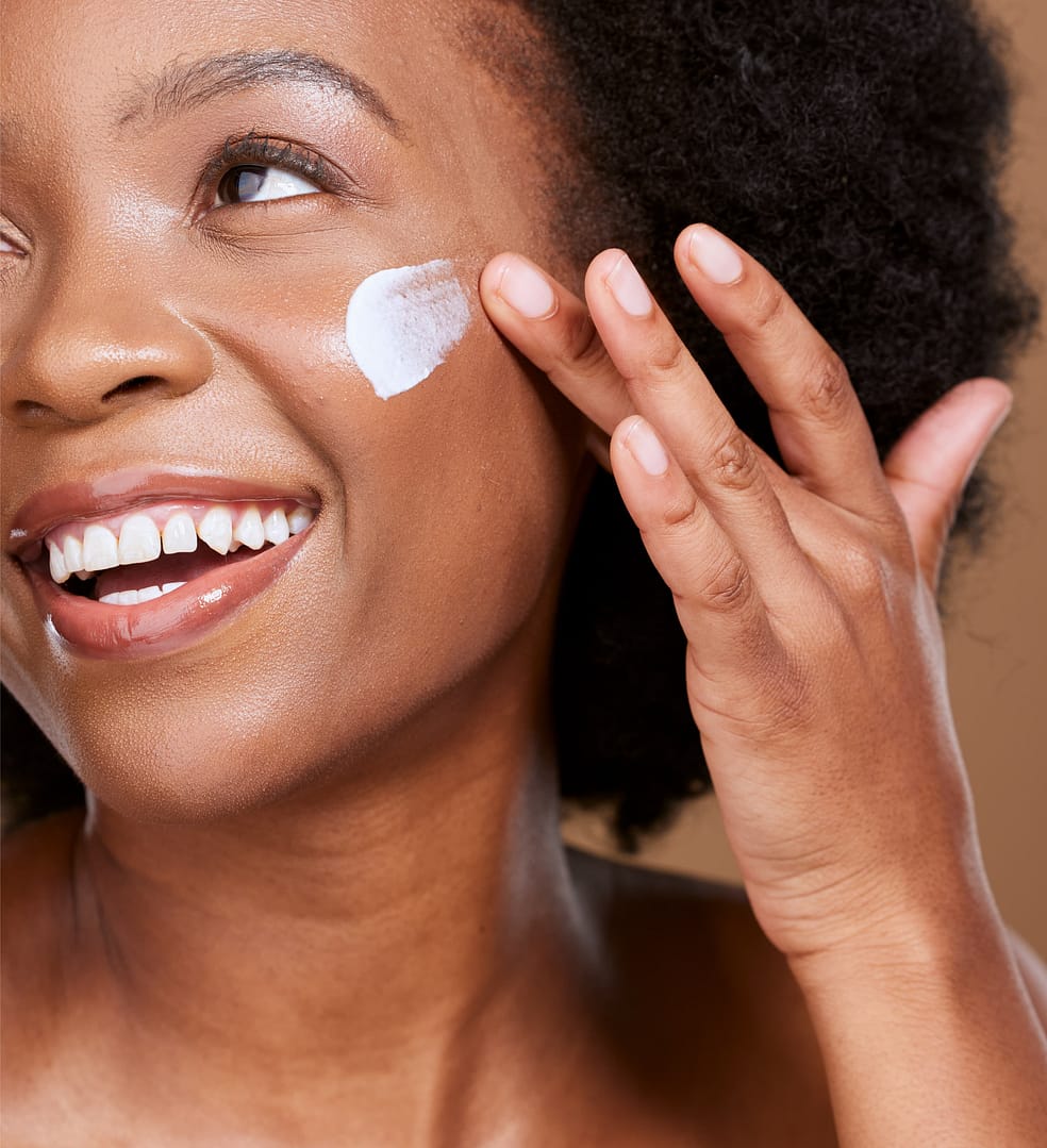 African American woman smiles gently while applying an acne spot treatment cream to her cheek