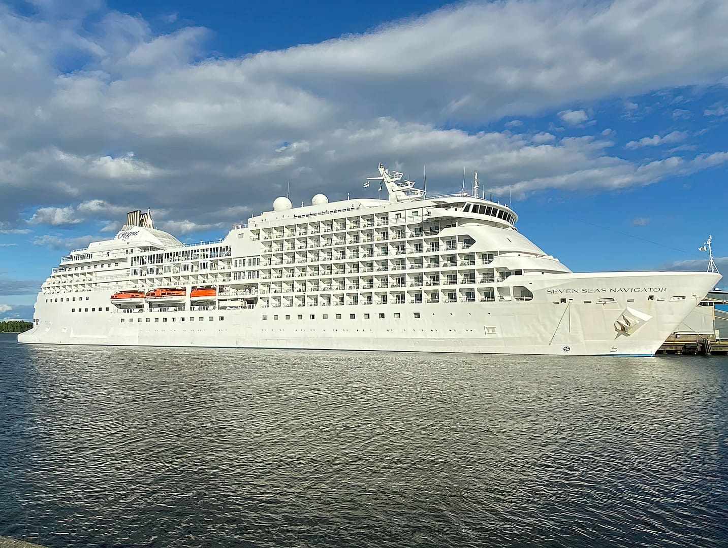 A large white Regent Seven Seas Navigator cruise ship docked in a calm harbor under a cloudy sky