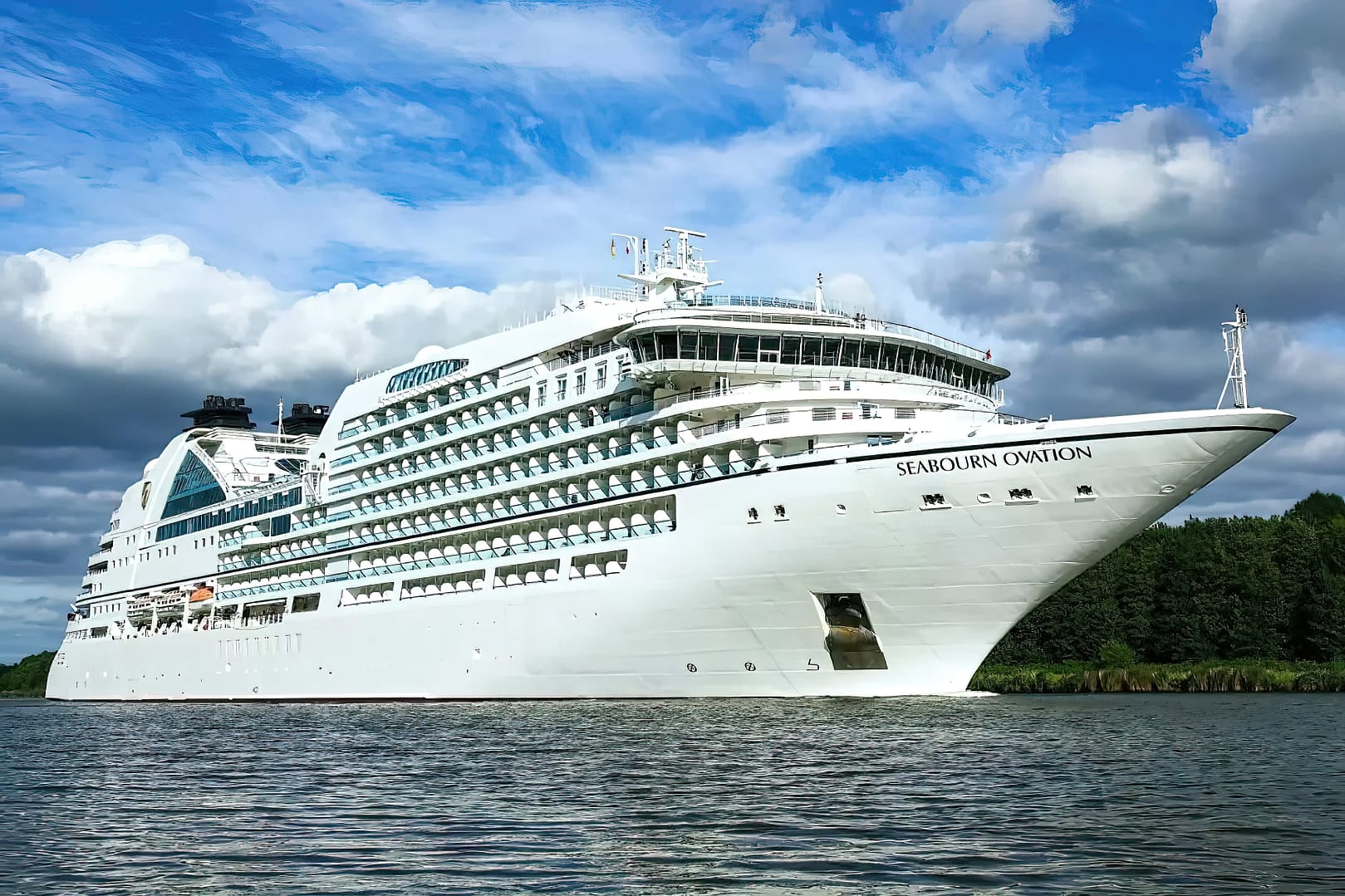 A large white Seabourn Ovation cruise ship on calm waters under a partly cloudy sky