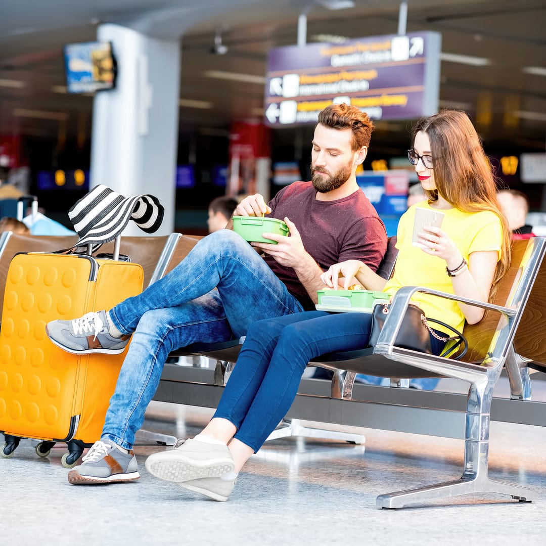Young couple having a snack with lunch boxes at the waiting hall of the airport during their vacation