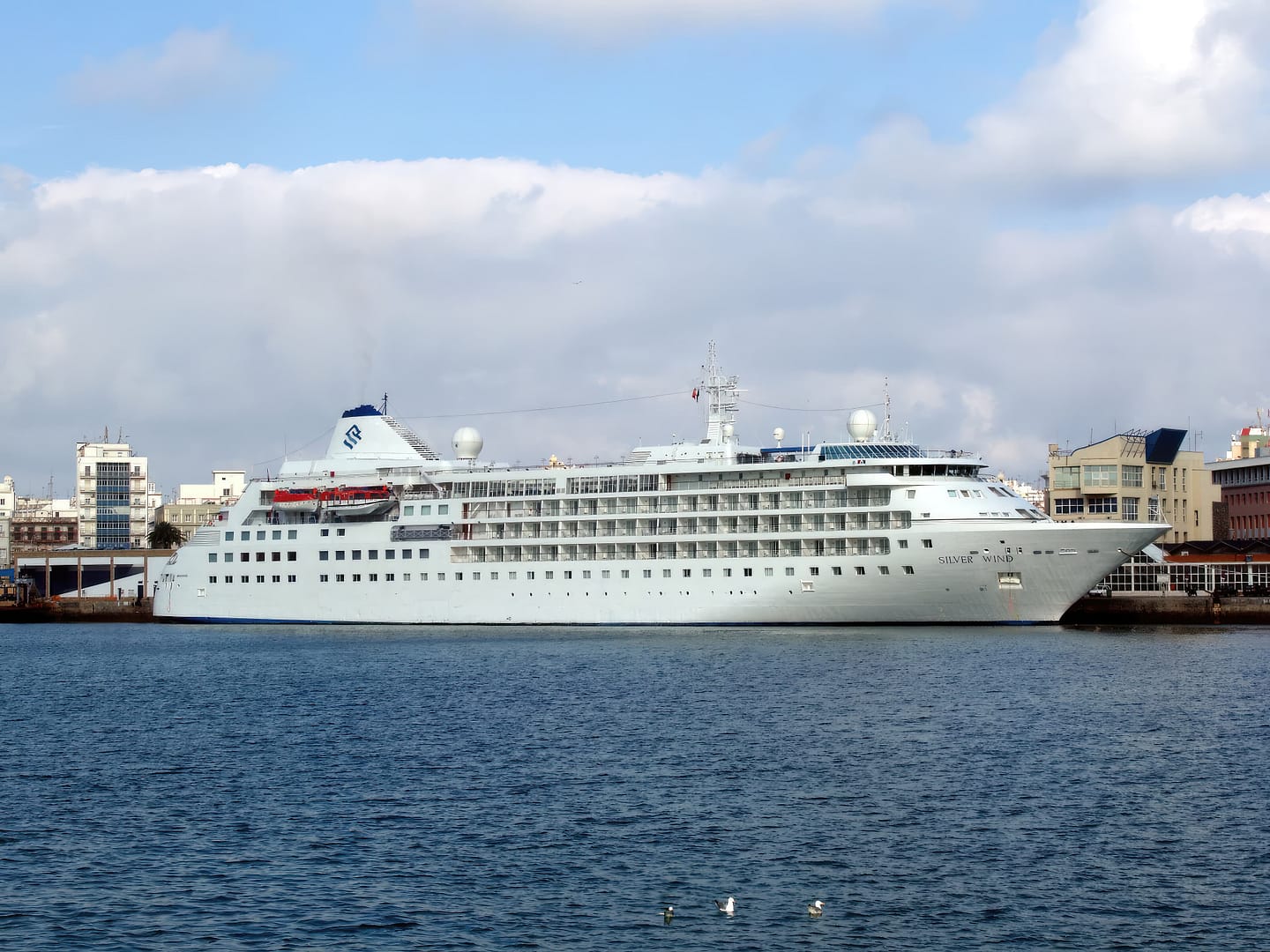 Silver Wind cruise ship docked in a harbor with city buildings in the background under a cloudy sky
