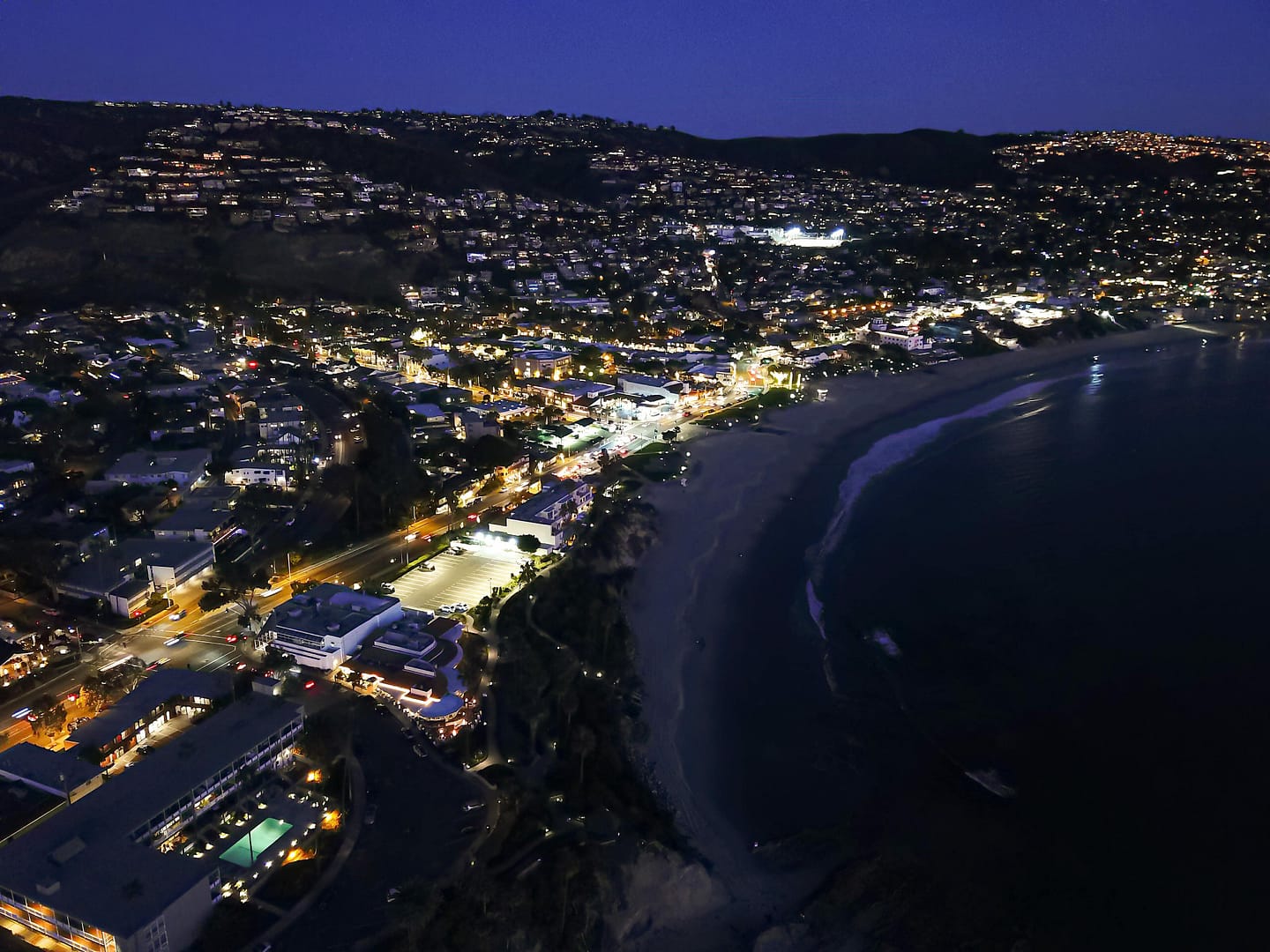 Aerial view of the beach and city in Laguna Beach at night, showcasing the mesmerizing beauty of the illuminated coastline