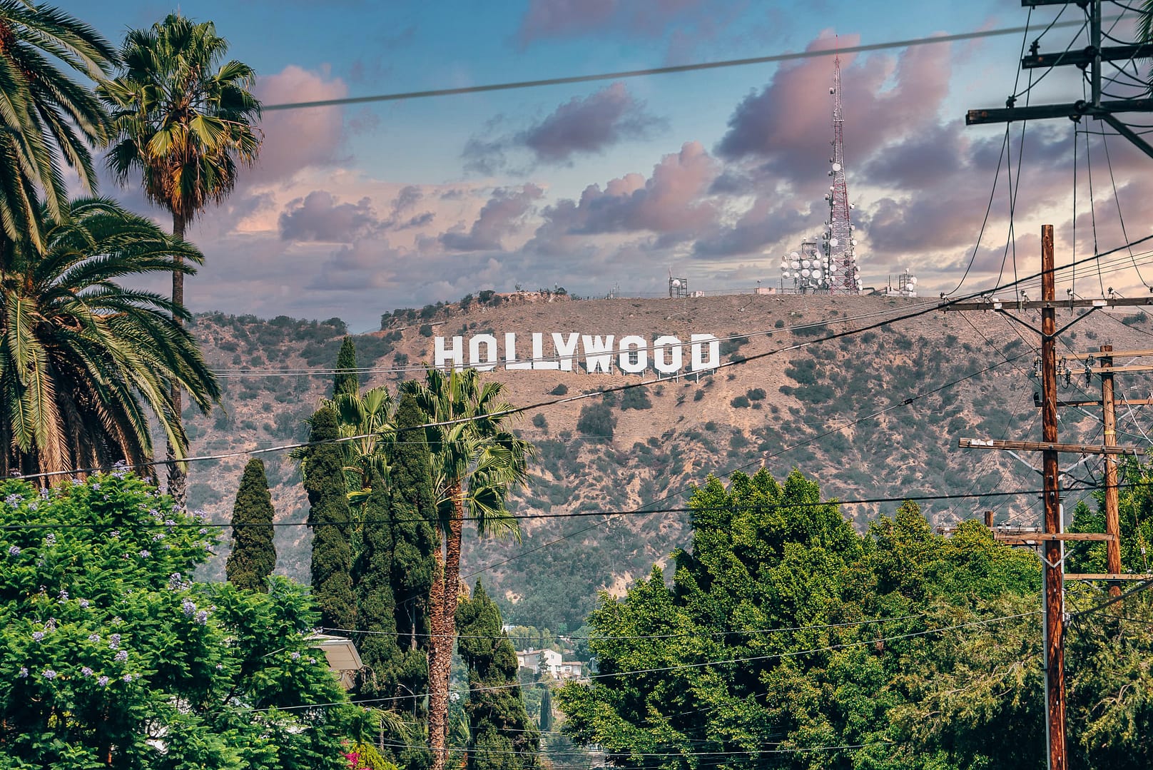 Hollywood sign on Mount Lee seen through electricity pole and trees on sunny day