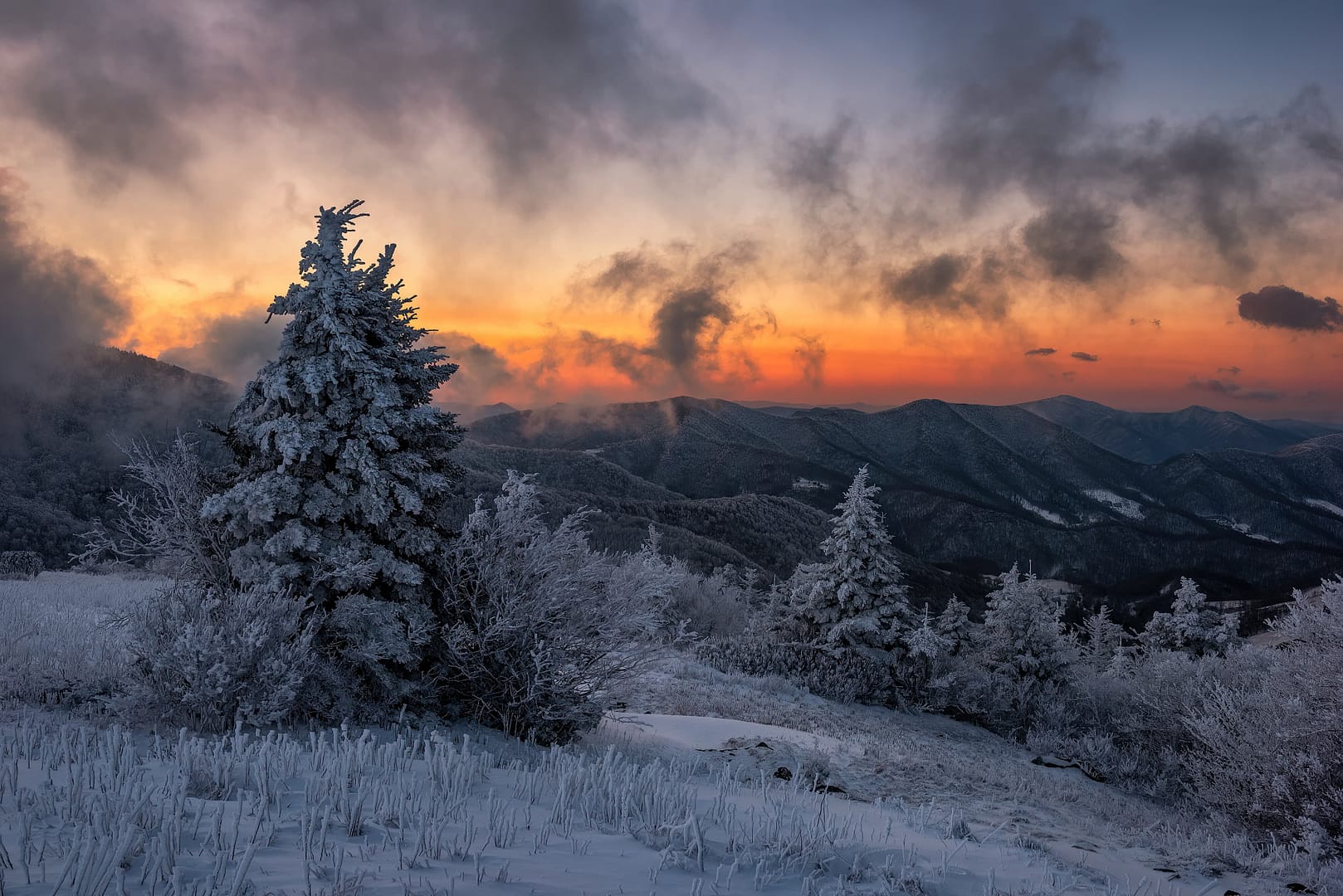 Snow-covered trees and landscape in Appalachian Trail, Tennessee at sunset with fiery orange and pink clouds in the sky over mountainous terrain
