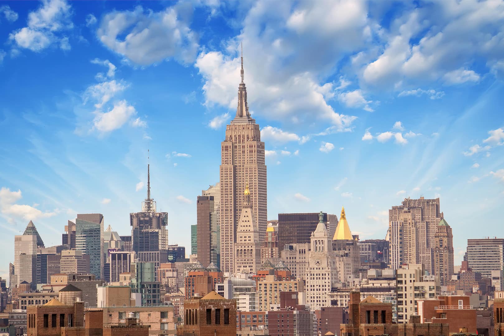 View of the New York City skyline with The Empire State Building dominating under a blue sky with fluffy clouds