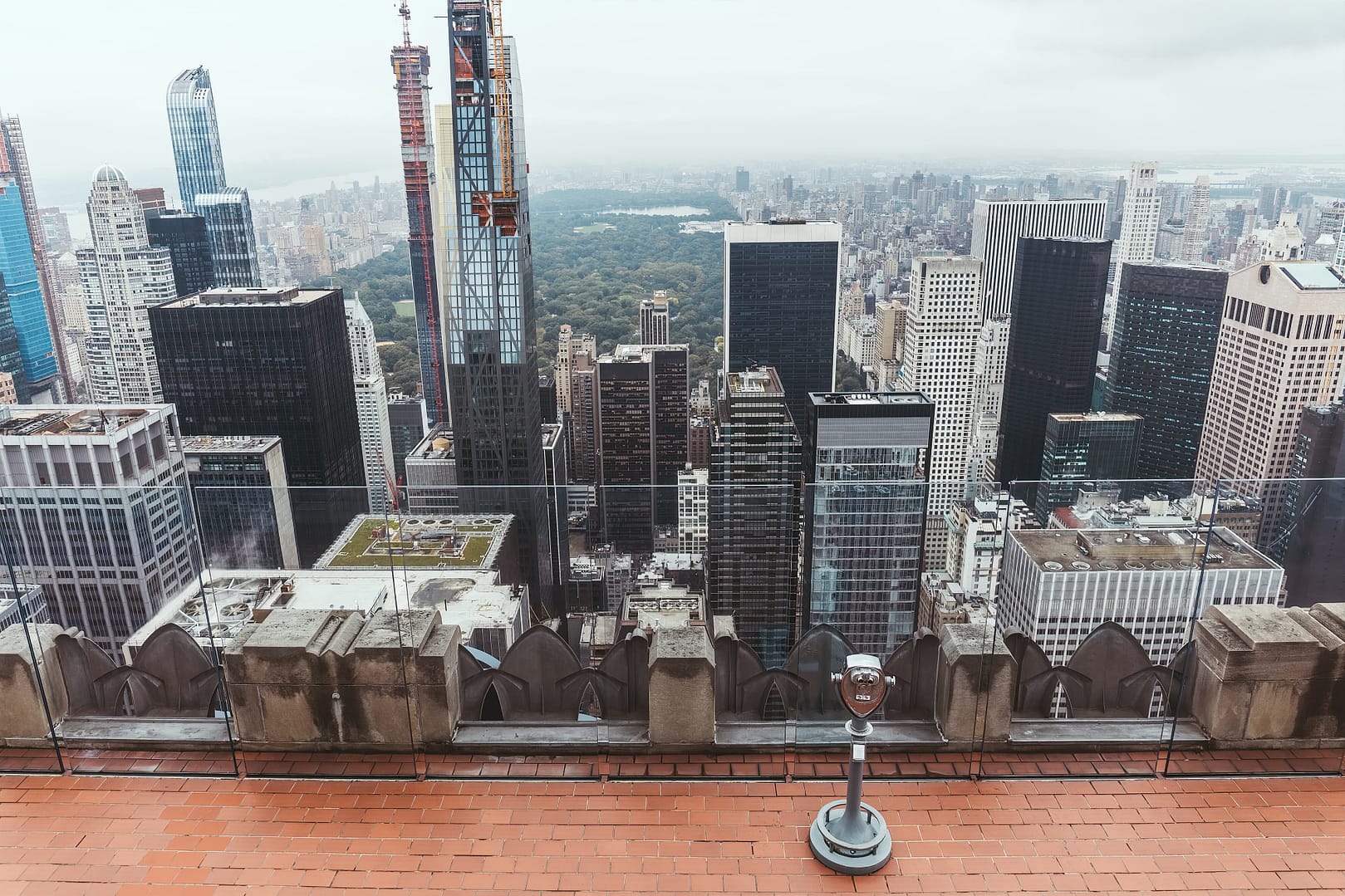 Aerial view of a cityscape with various skyscrapers and a large park in the background, taken from the Top of the Rock Observation Deck on a cloudy day