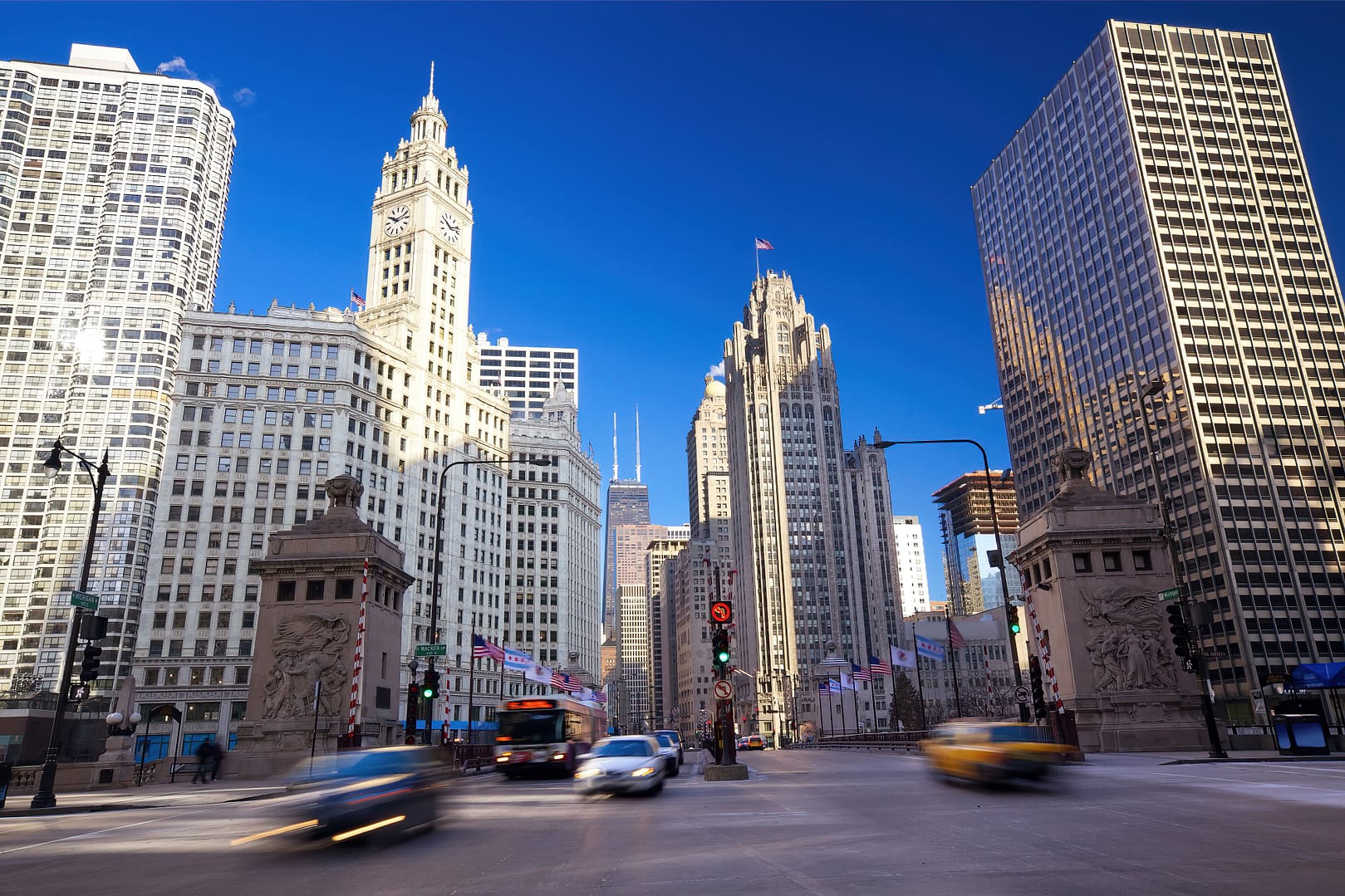 Downtown Chicago, encompassing The Magnificent Mile with historic buildings and modern skyscrapers, features busy traffic at dusk under a clear blue sky