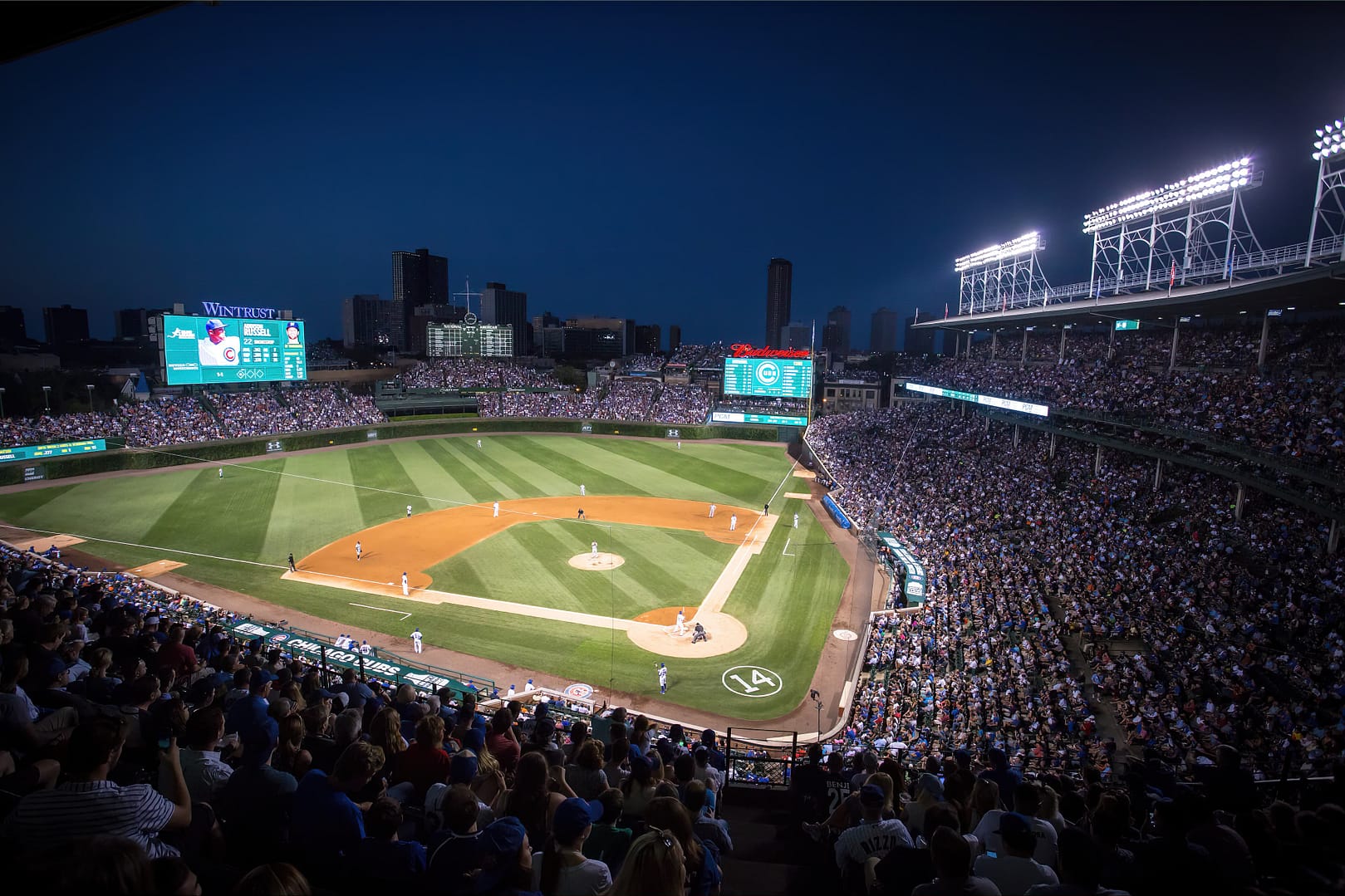 Nighttime view of a crowded Wrigley Field with illuminated field and scoreboards during a game