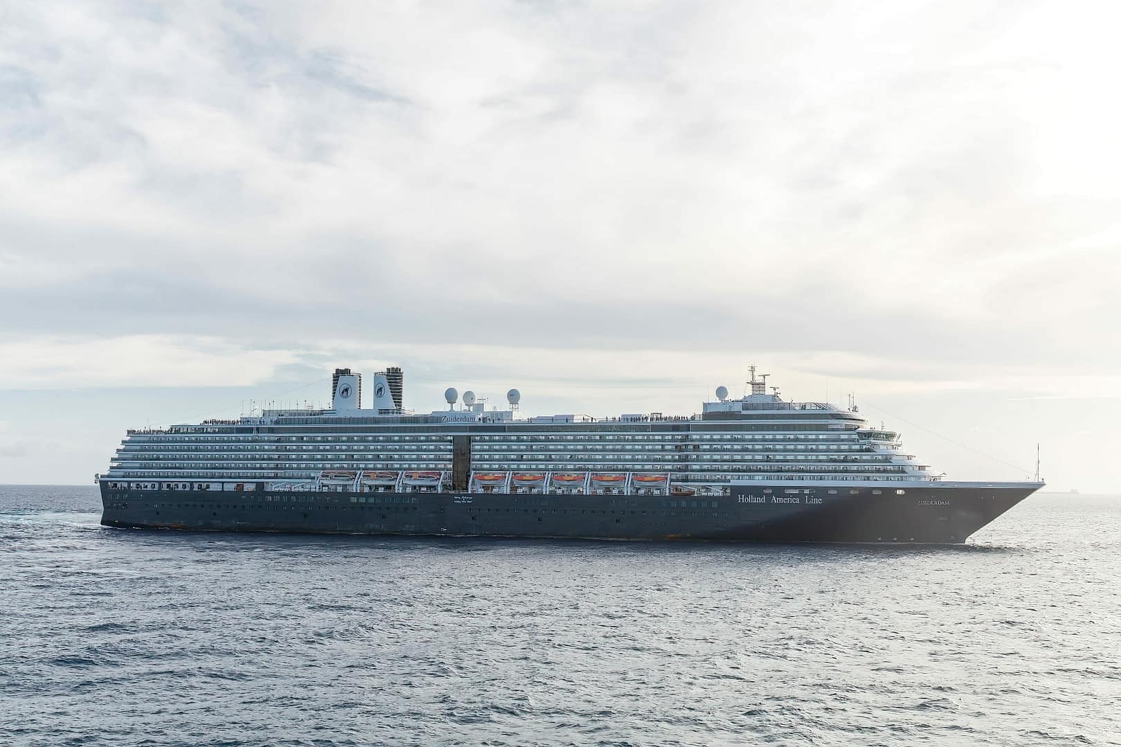 Holland America Line cruise ship sailing on the ocean under a bright sky