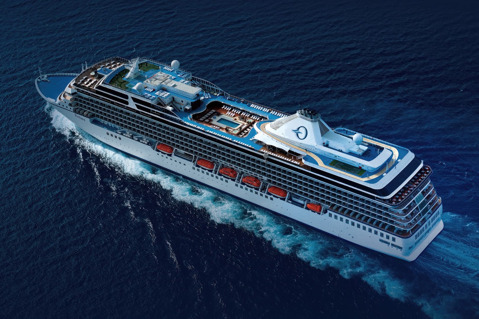 Aerial view of a large Oceania Cruises cruise ship sailing in deep blue ocean waters, featuring multiple decks and swimming pools