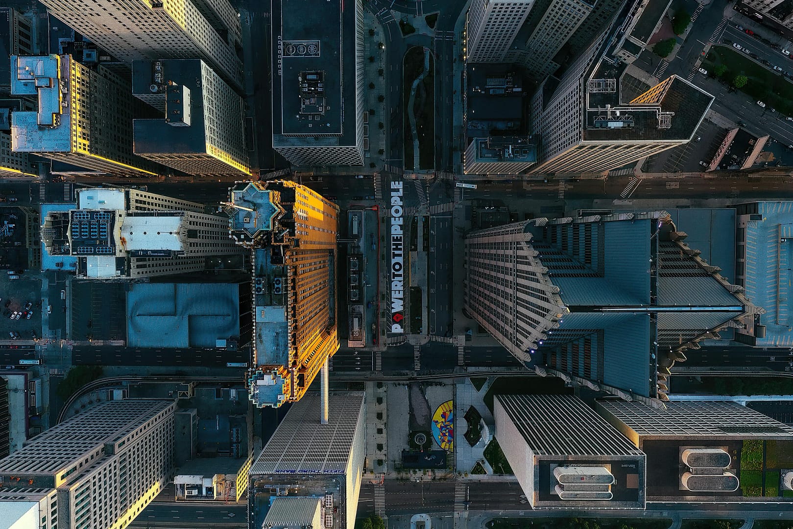 Aerial view of a Detroit city intersection with tall buildings surrounding it. The words "POWER TO THE PEOPLE" are painted on the street