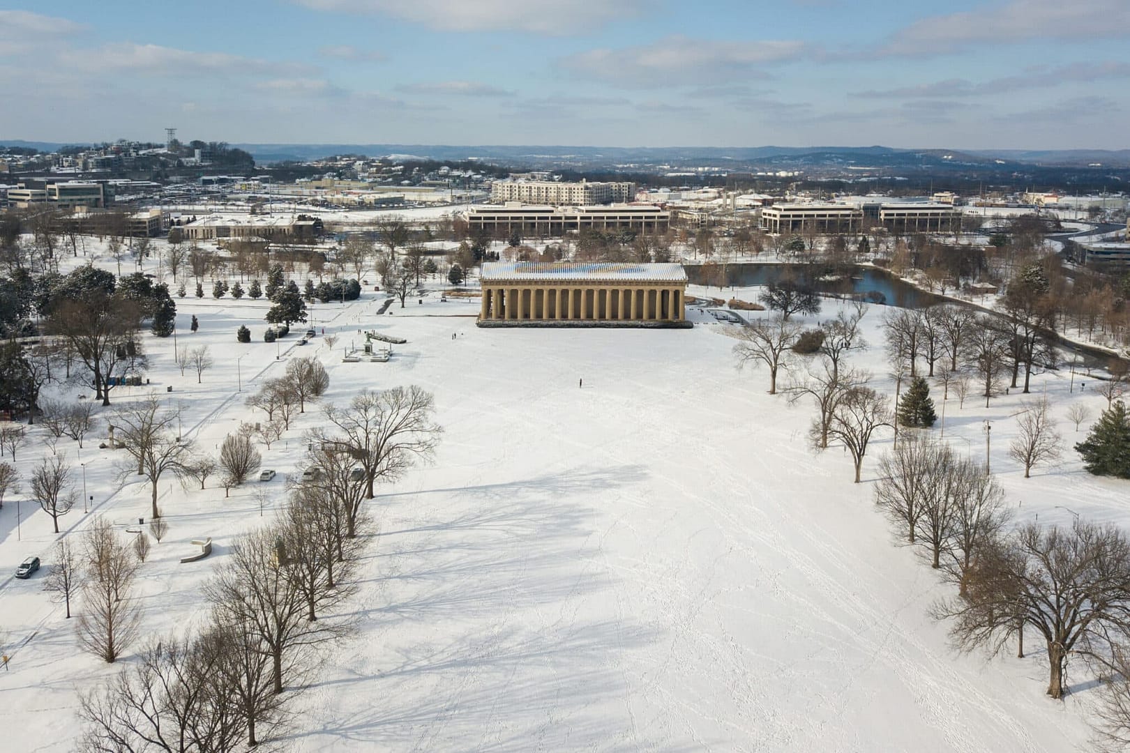 A scenic view of a snow-blanketed field surrounded by trees and buildings in the background