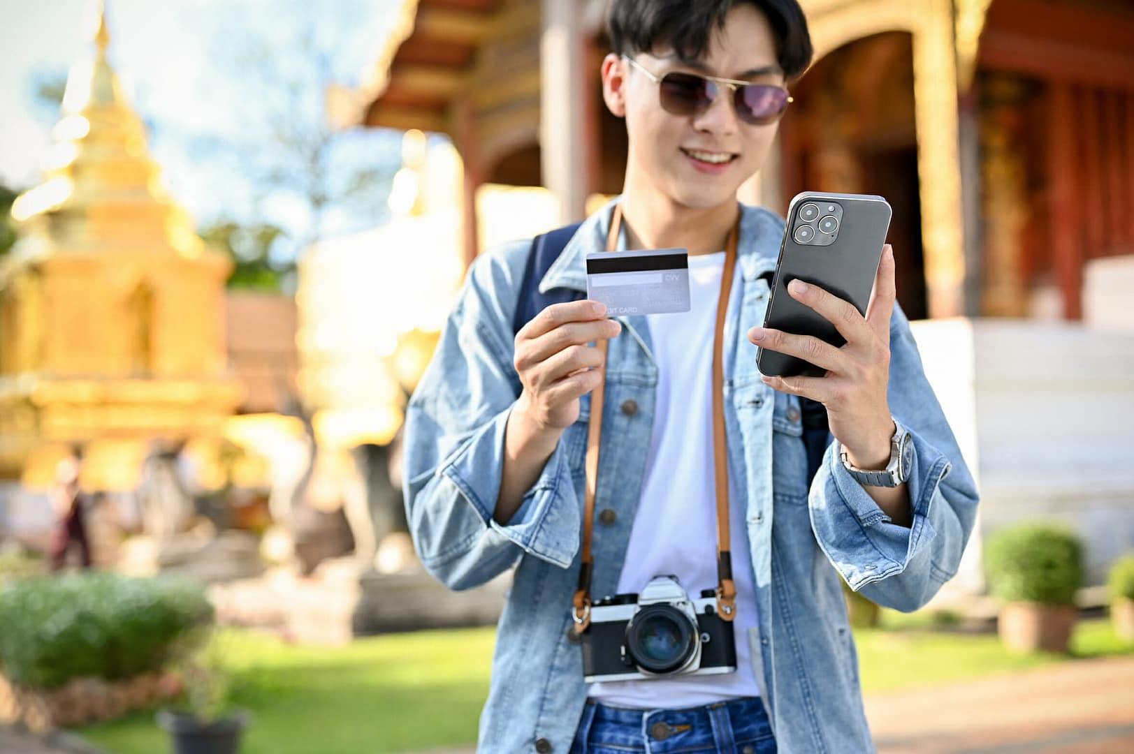 Asian male tourist using his mobile banking application while visiting beautiful temple