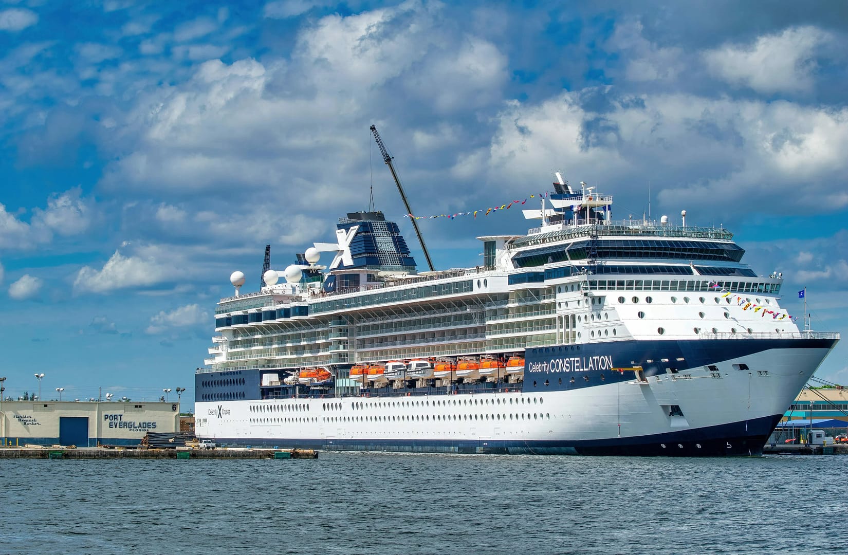 Large Celebrity Constellation cruise ship docked at a port under a blue sky with fluffy clouds